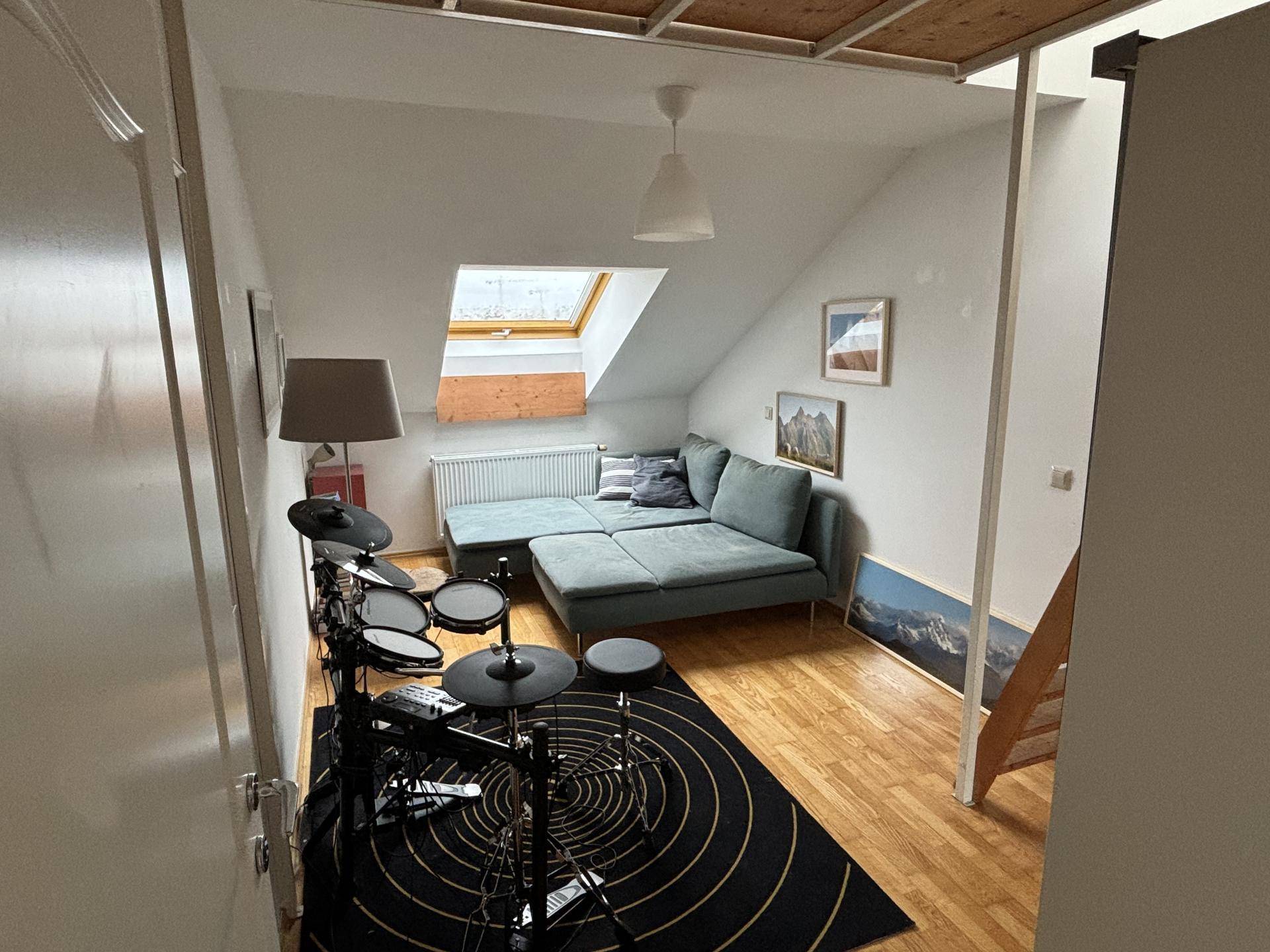 Gemütlicher Wohnbereich im Dachgeschoss mit Sofa, Dachfenster und Holzboden.