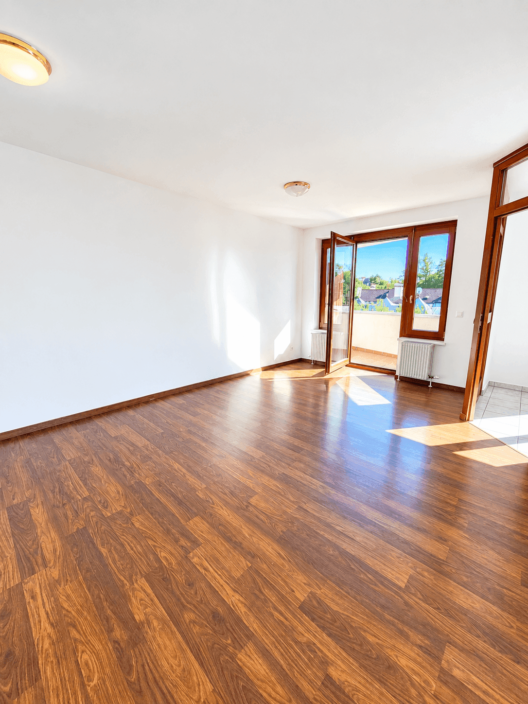 Helles Wohnzimmer mit Laminatboden und Zugang zu einem Balkon, der viel Tageslicht hereinlässt.