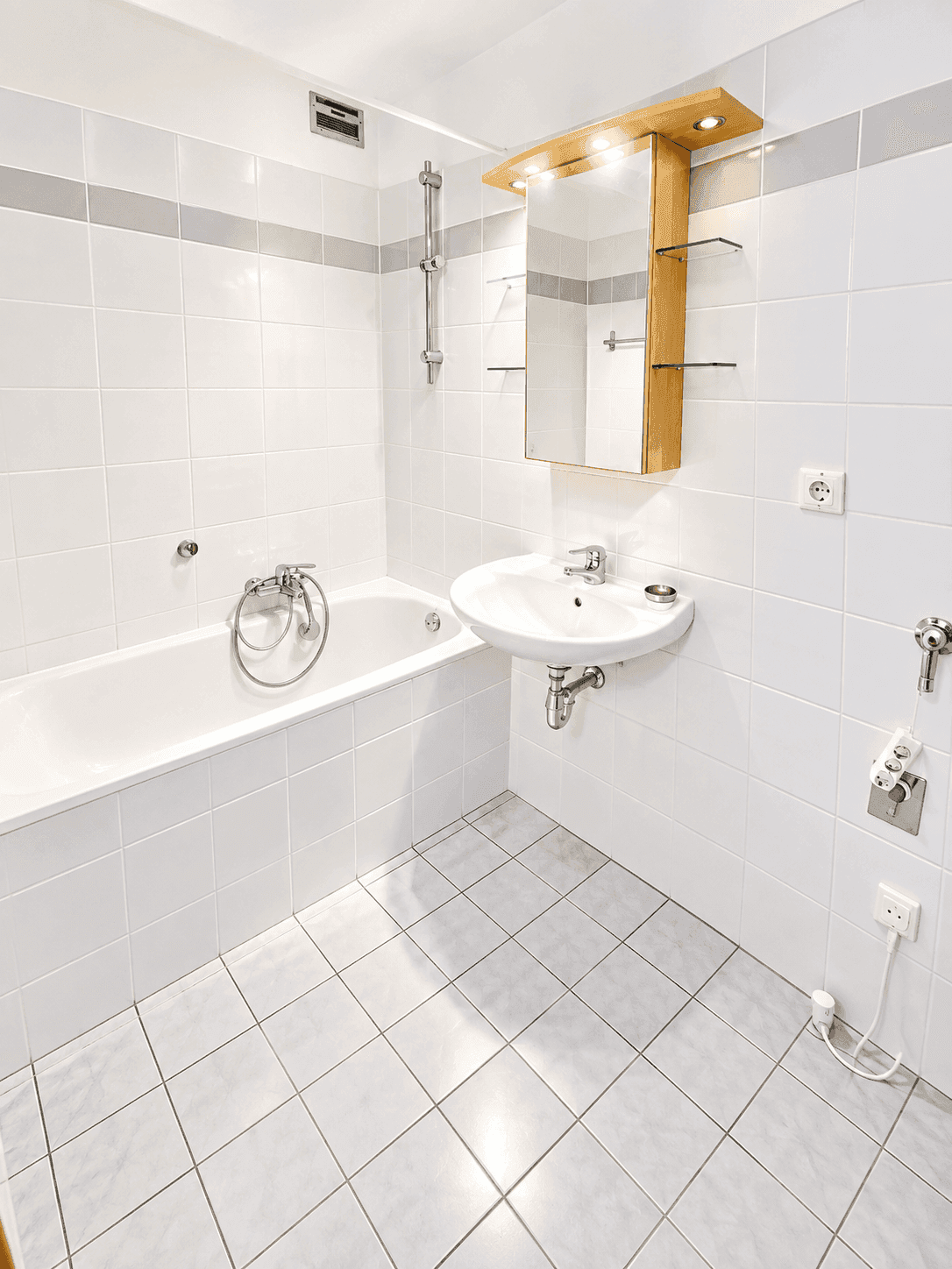 Gefliestes Badezimmer mit Badewanne, Waschbecken und Spiegelschrank in hellem Design.