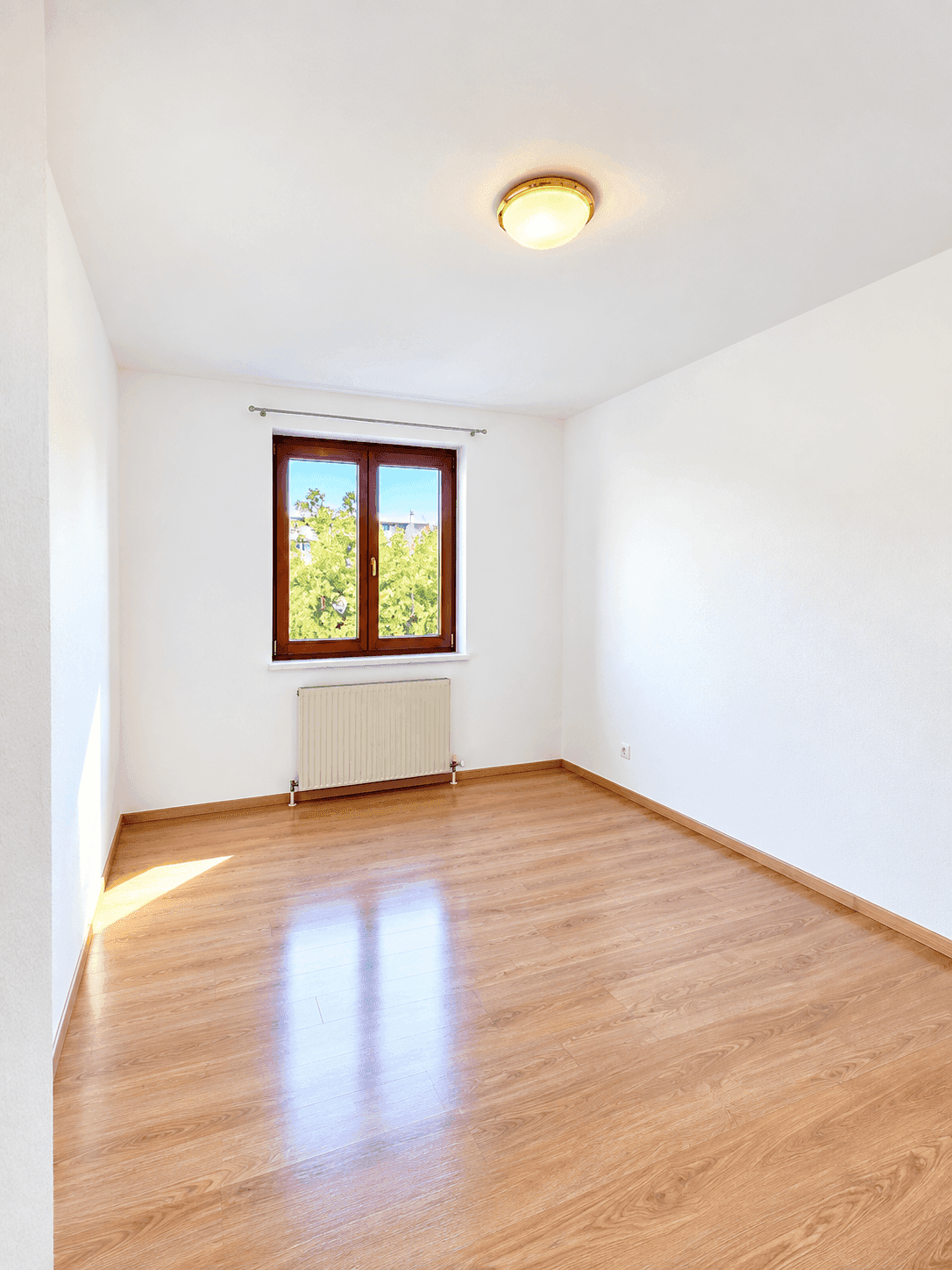 Helles Zimmer mit Laminatboden und einem Fenster, das viel natürliches Licht hereinlässt.