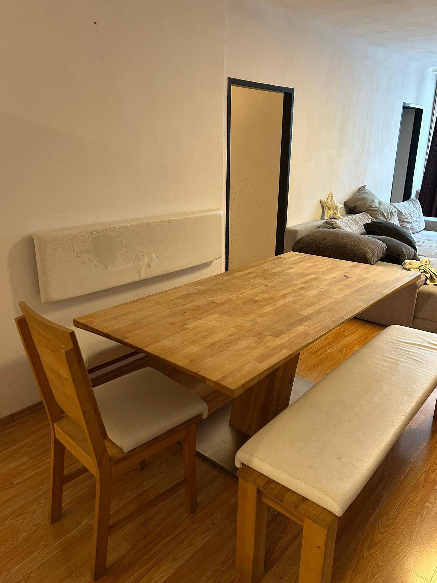 Essbereich mit Holztisch, Bank und Stuhl, angrenzend an einen Wohnbereich mit Sofa.