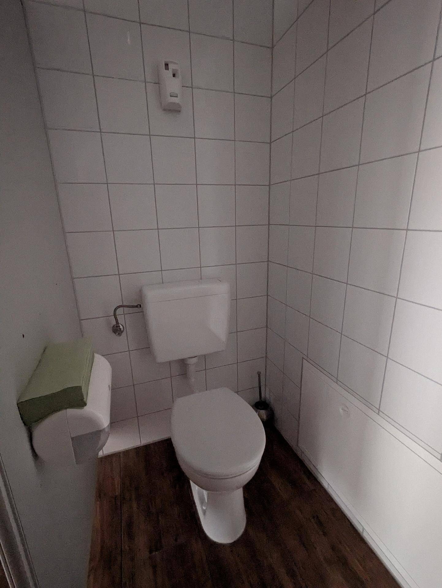 Separate Toilette mit WC, weißen Wandfliesen und Laminatboden.