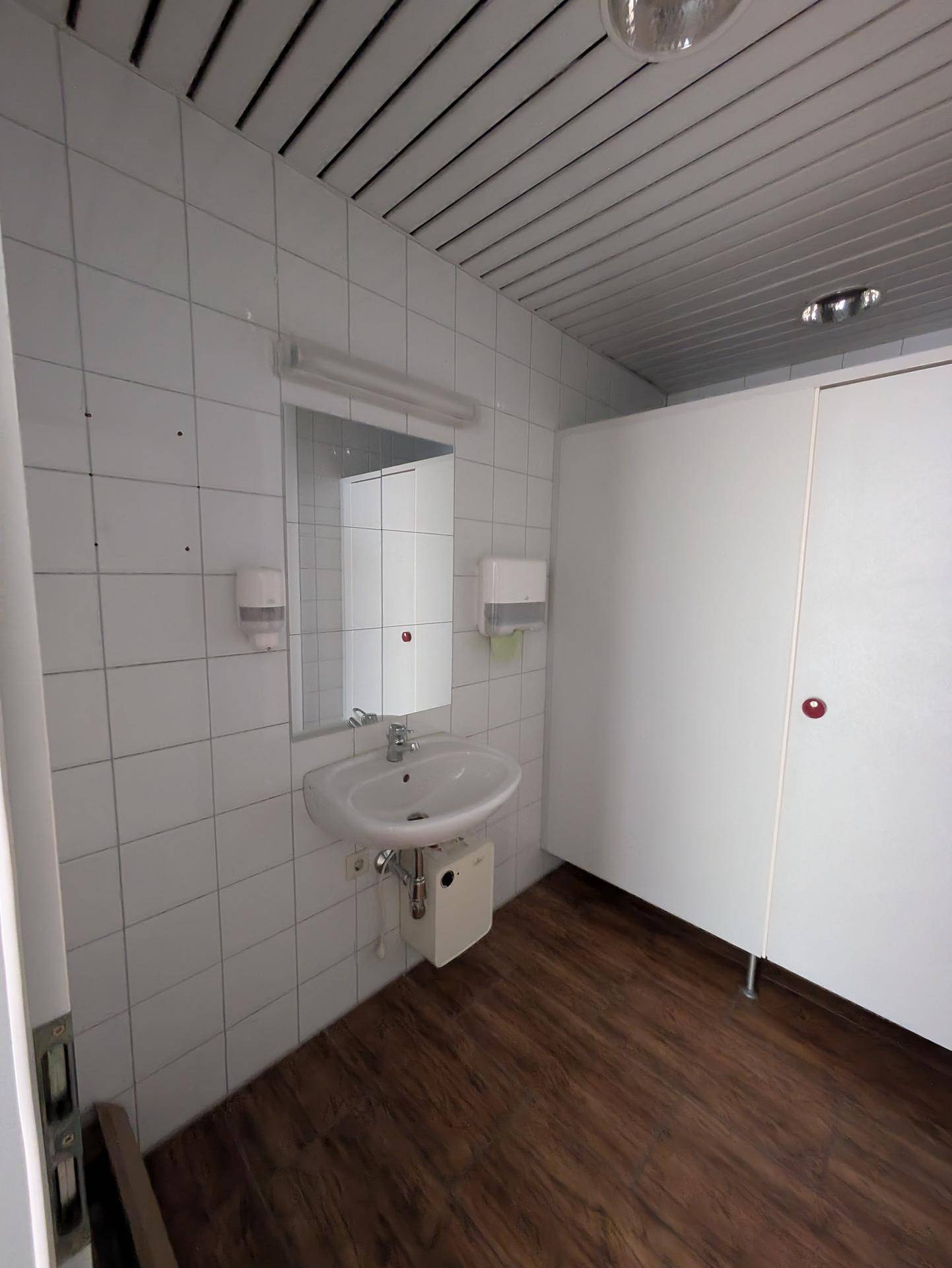 Badezimmer mit Waschbecken, Spiegel und weißen Fliesen an den Wänden.