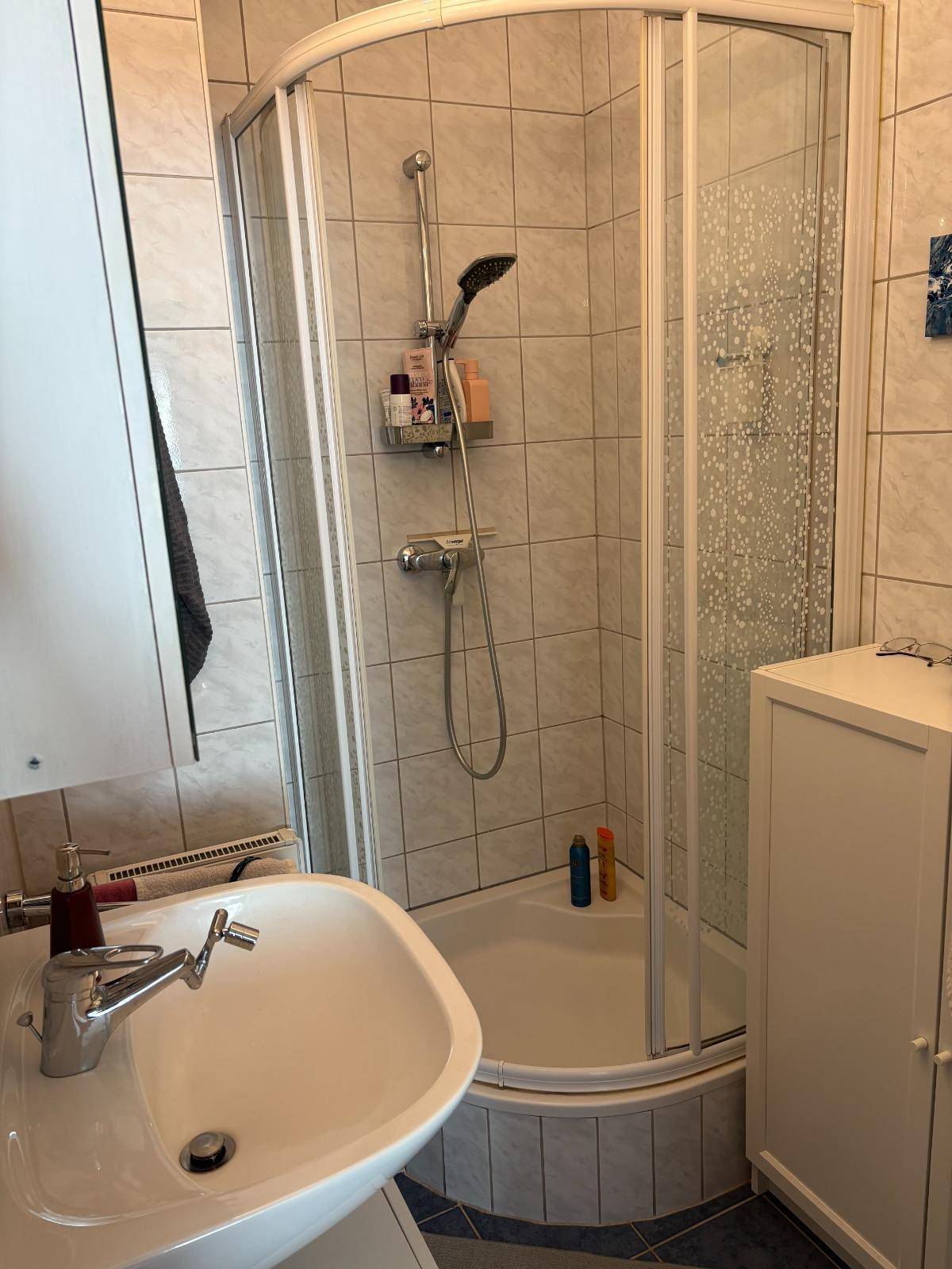 Badezimmer mit Eckdusche, Waschbecken und hellen Fliesen.