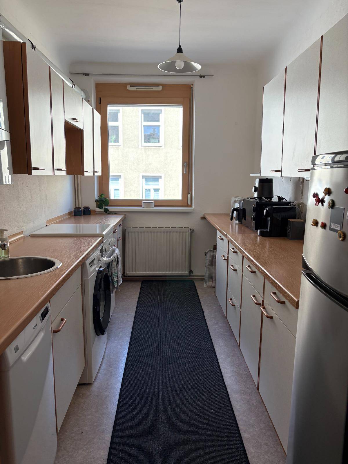 Funktionale Küche mit weißen Schränken, Holz-Arbeitsplatten und Fenster.