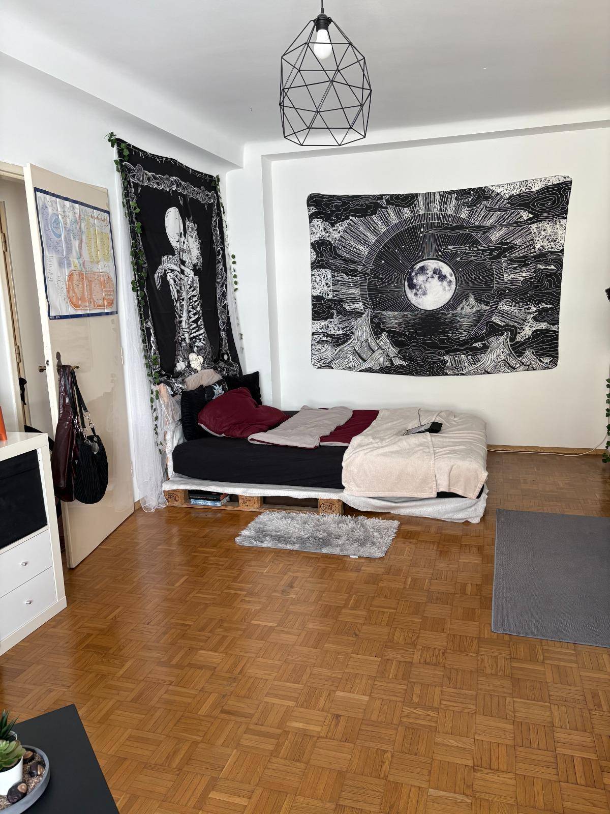 Schlafzimmer mit Palettenbett, Holzboden und dekorativen Wandteppichen.