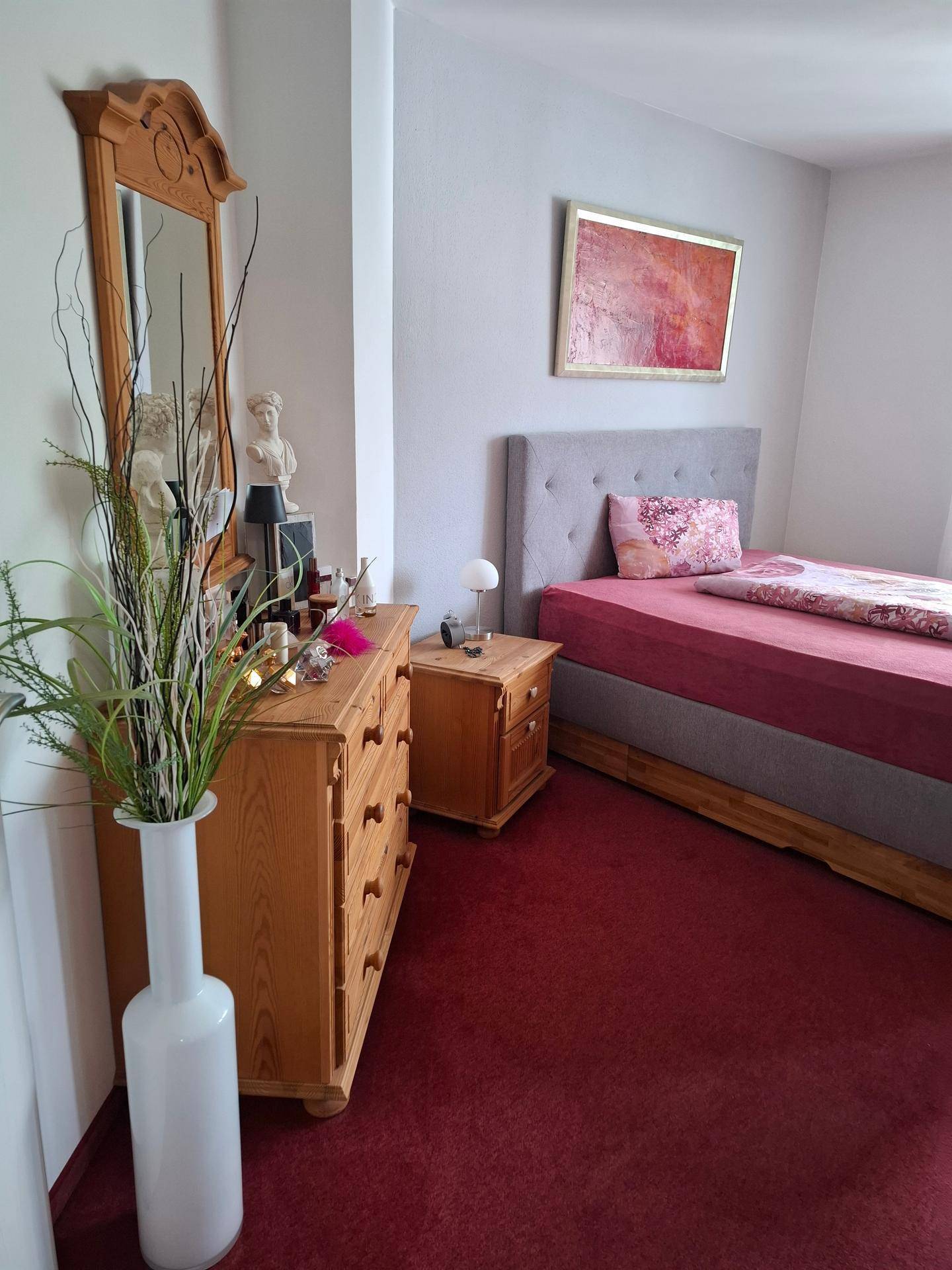 Schlafzimmer mit Einzelbett, rustikaler Holzkommode und einem großen Spiegel.