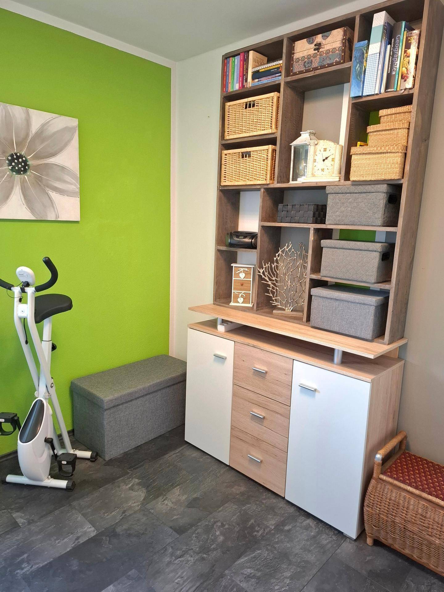 Zimmer mit grünen Wänden, einem Bücherregal und einem Heimtrainer für sportliche Aktivitäten.