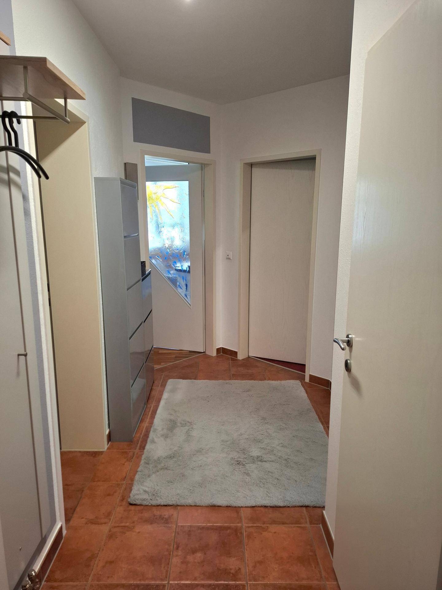 Heller Flur mit Terrakotta-Fliesenboden, einem Schuhschrank und einem weichen Teppich.