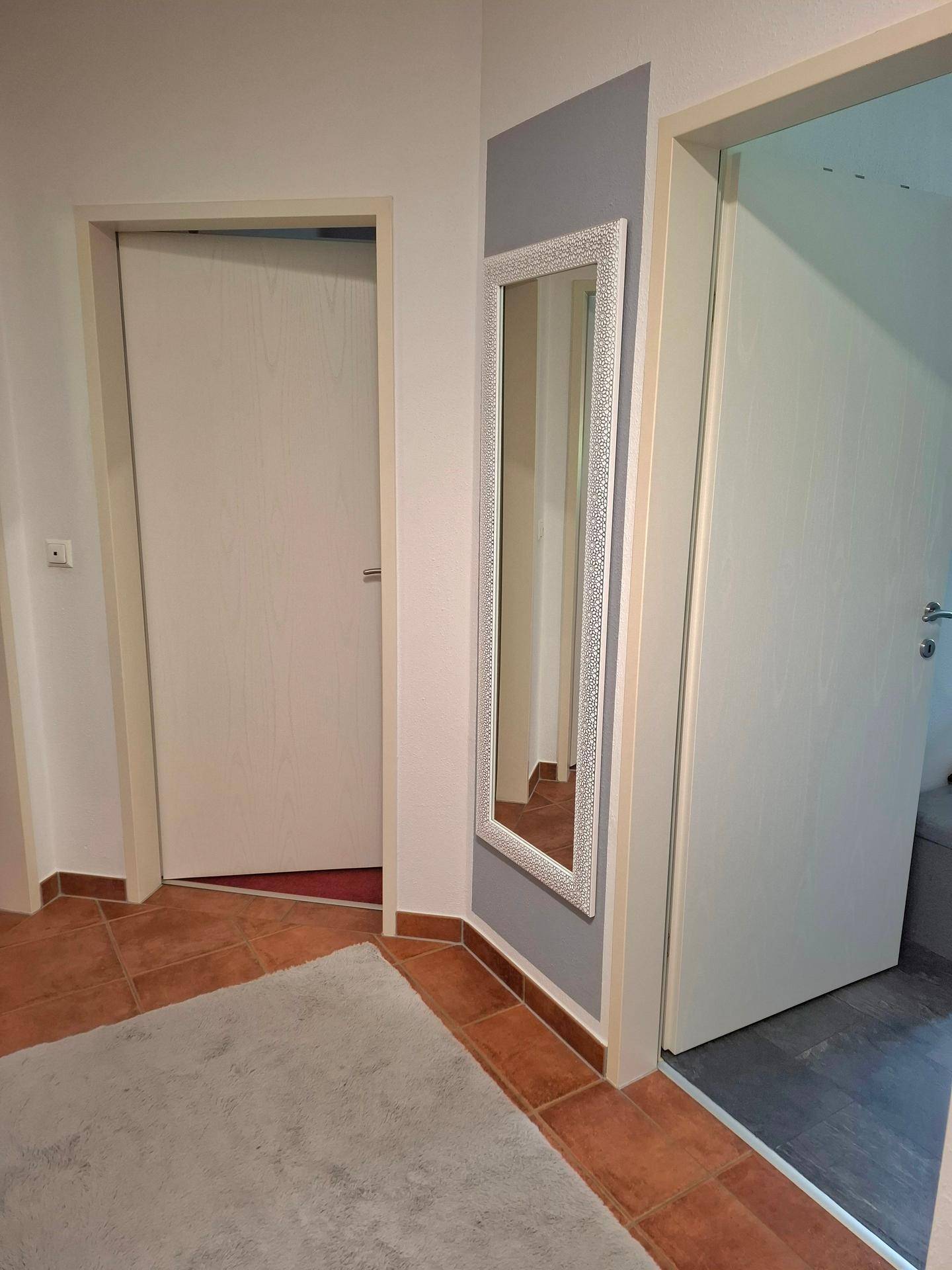 Eingangsbereich mit einem dekorativen Spiegel an der Wand und Terrakotta-Fliesenboden.