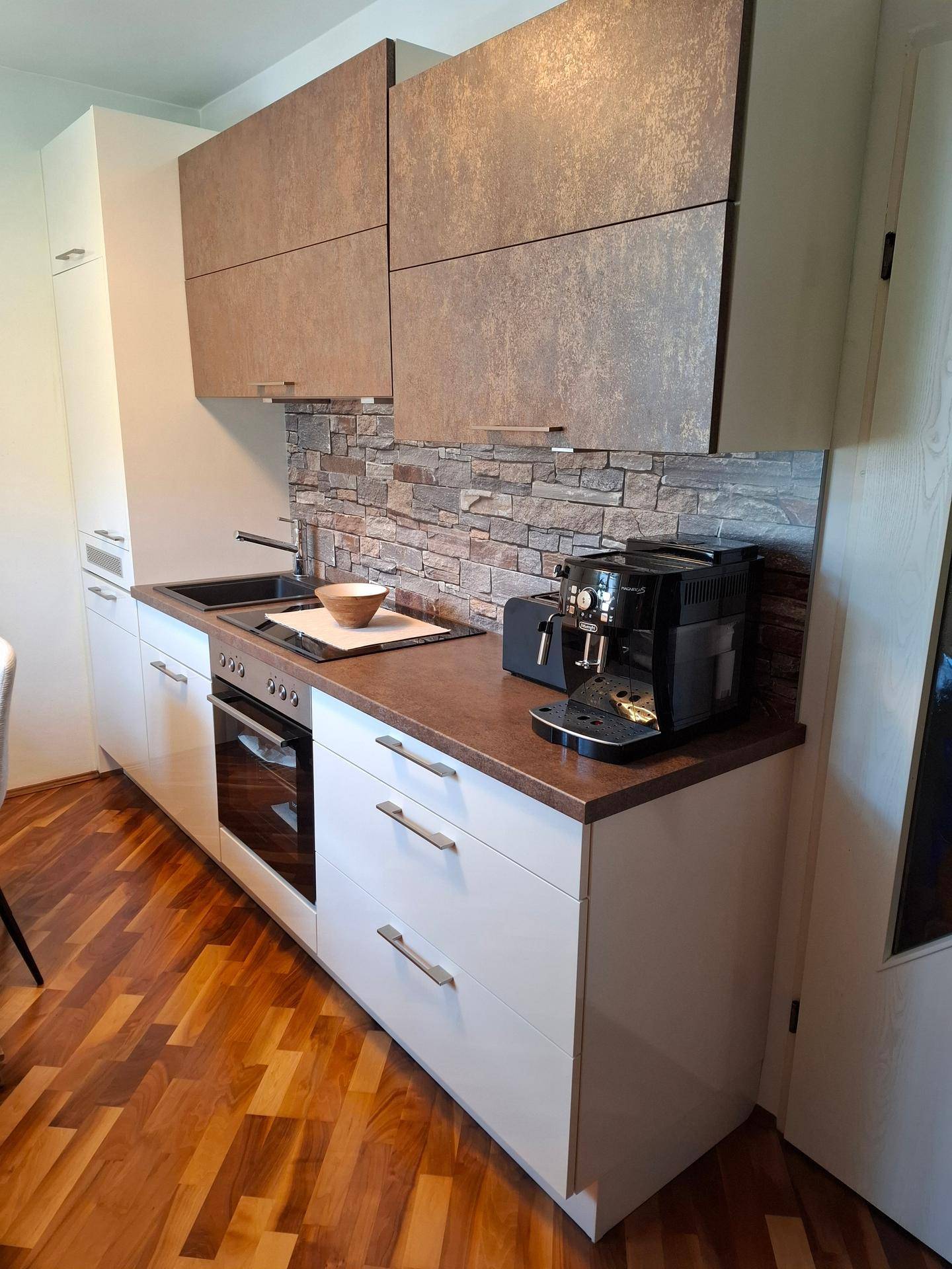 Moderne Küche mit weißen Unterschränken, braunen Oberschränken und einer Steinoptik-Rückwand.