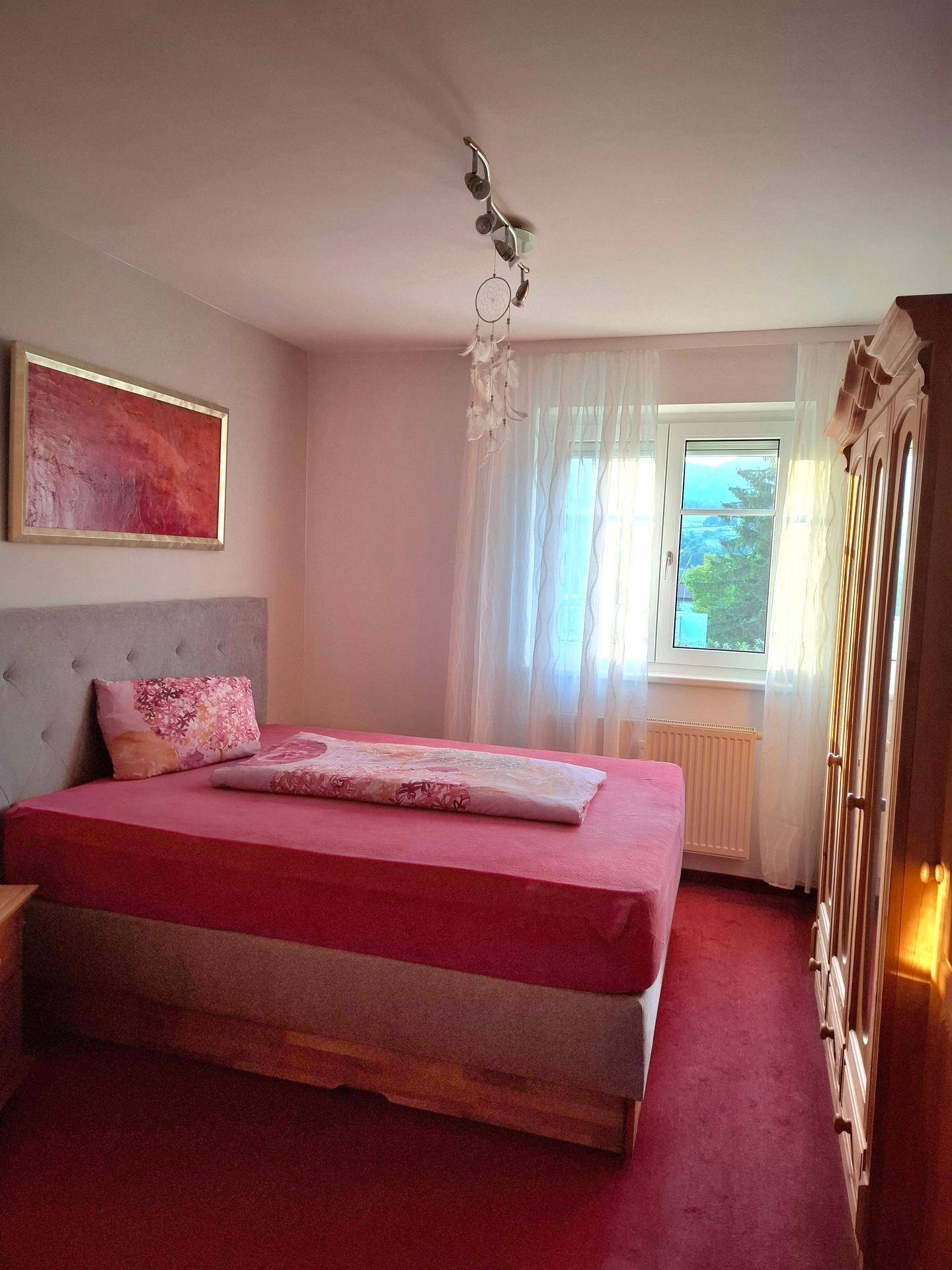 Helles Schlafzimmer mit Einzelbett, Holzschrank und Fenster mit Blick ins Grüne.
