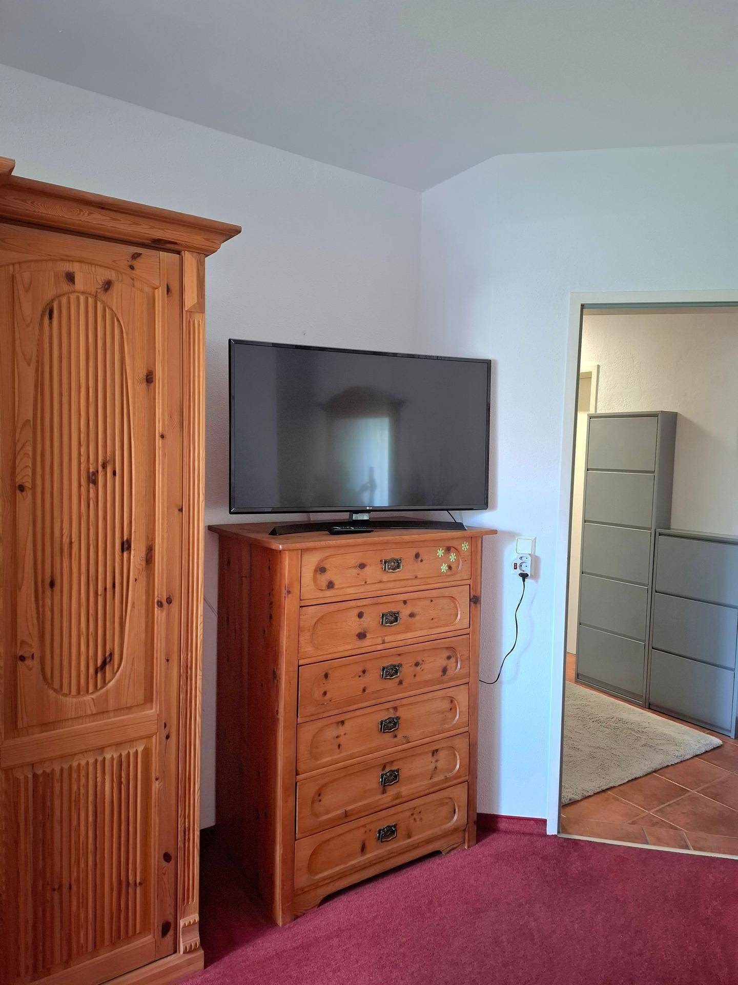 Schlafzimmer mit großem Holzschrank, Kommode und einem Fernseher.
