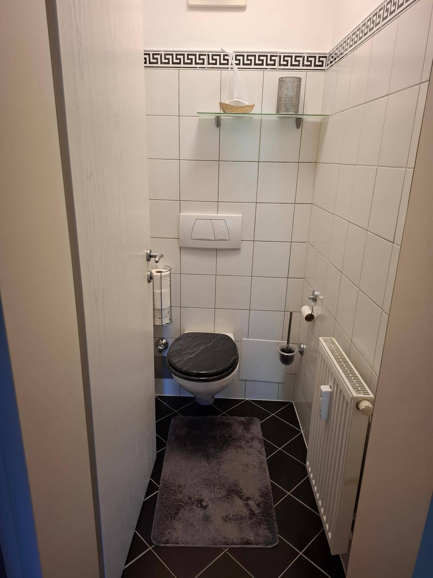Kleines Gäste-WC mit Wand-WC, Fliesenboden und einem Heizkörper.
