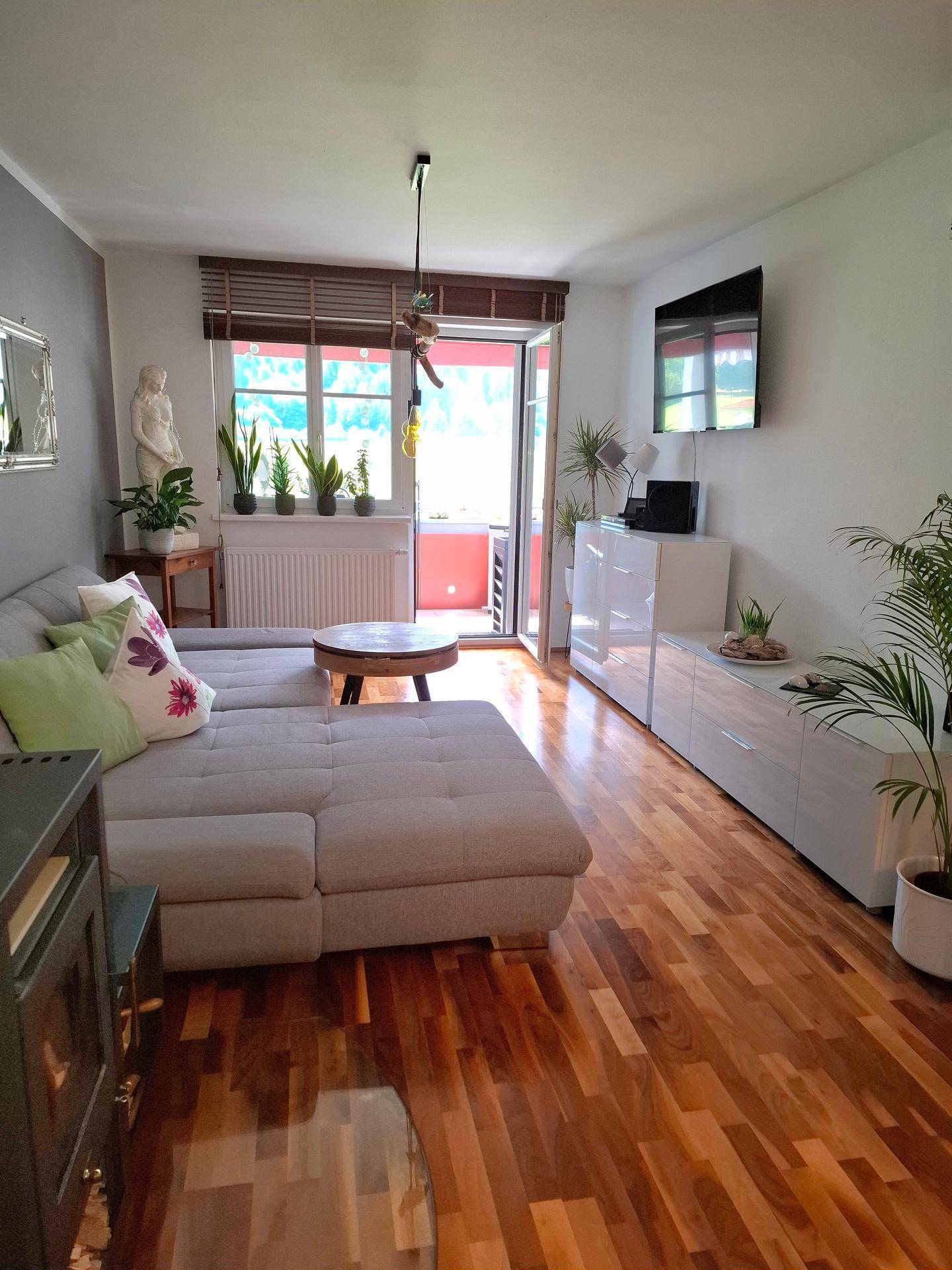 Gemütliches Wohnzimmer mit großem Sofa, Fernseher und Zugang zum Balkon.