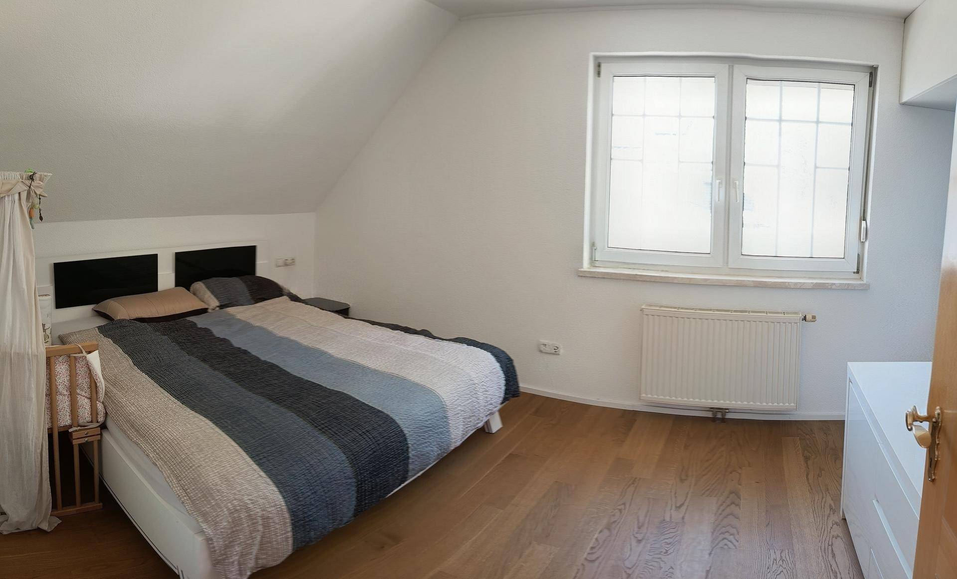 Schlafzimmer im Dachgeschoss mit Holzboden, Doppelbett und Fenster.