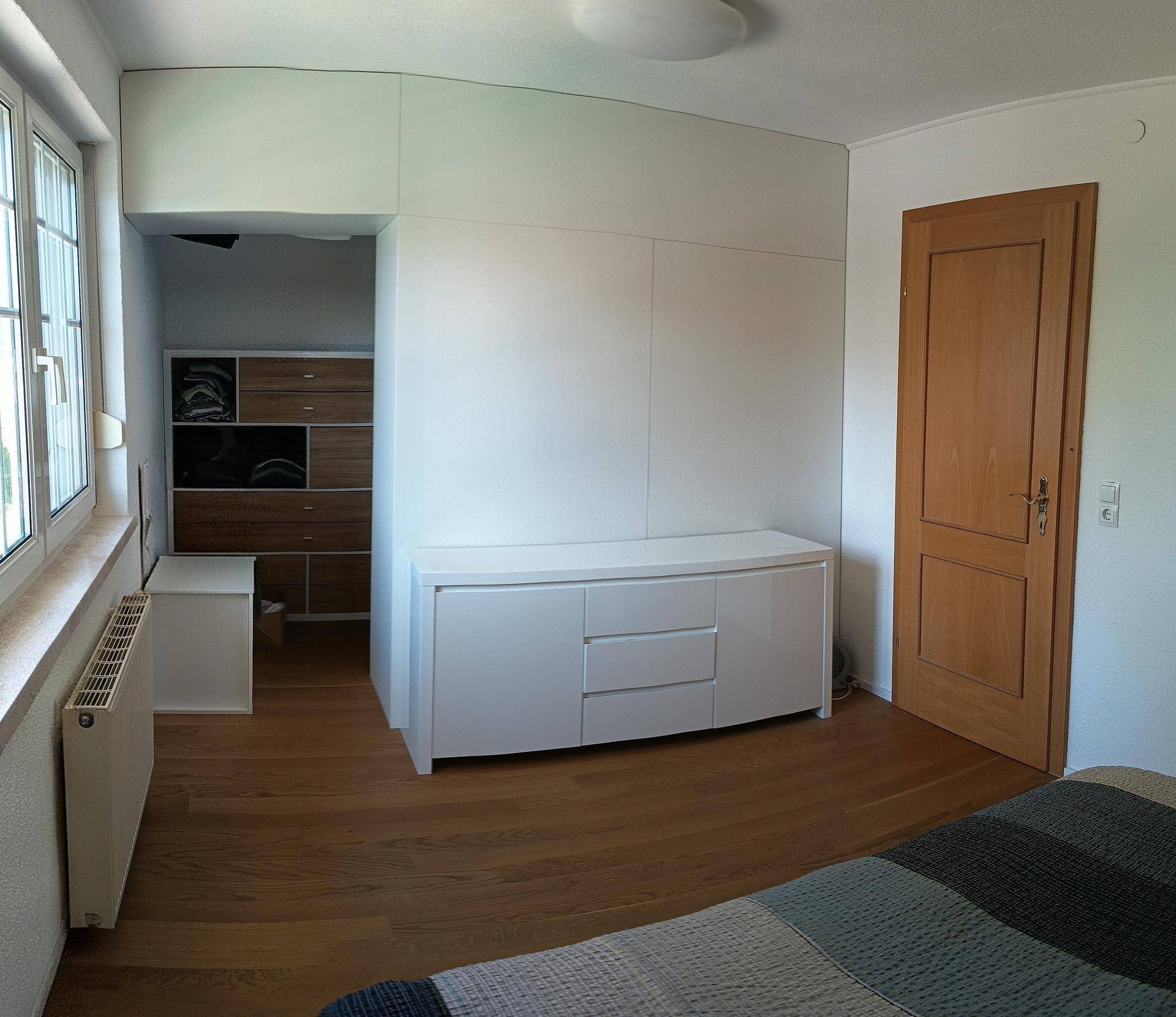 Schlafzimmer mit Holzboden, Einbauschränken und Zugang zu einem begehbaren Kleiderschrank.