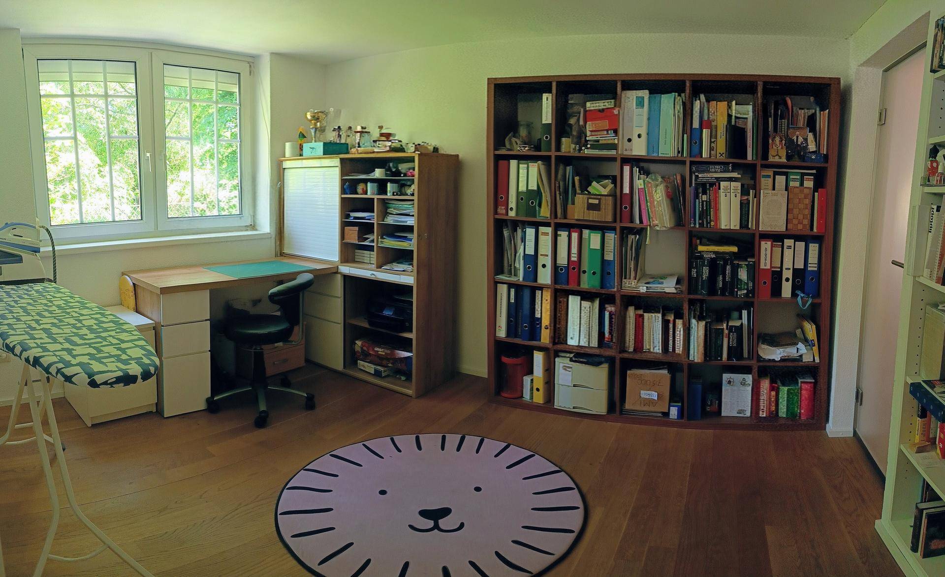 Helles Arbeitszimmer mit großem Bücherregal, Schreibtisch und Holzboden.