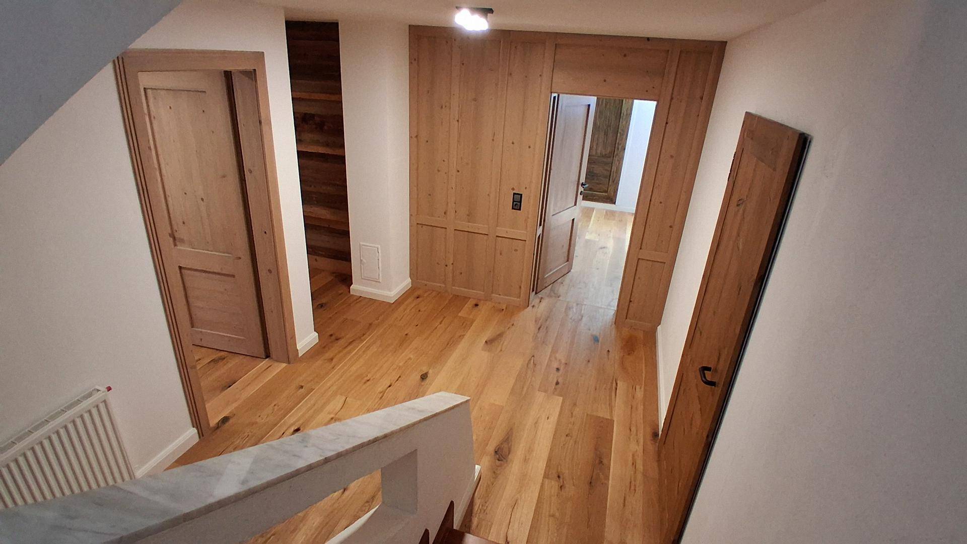 Heller Flur mit breiten Holzplanken, Holztüren und integrierten Holzschränken, die eine warme Atmosphäre schaffen.