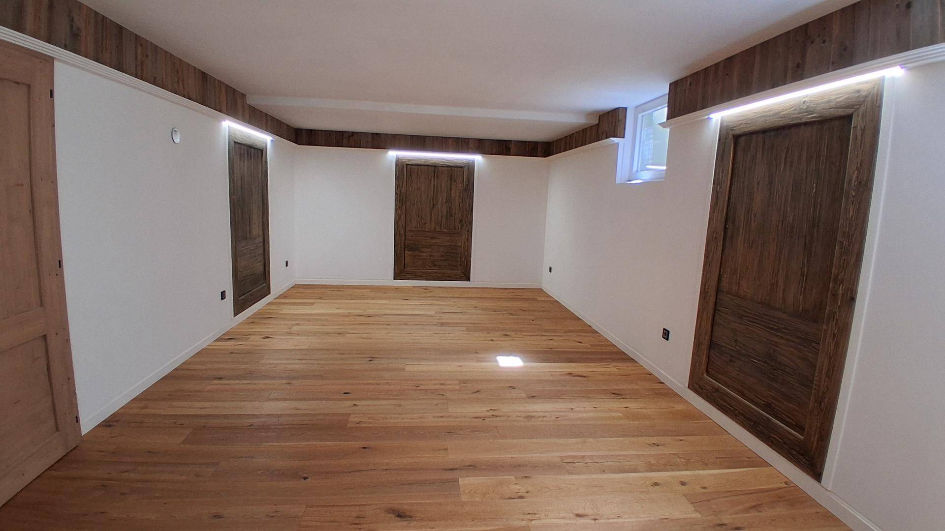 Großes, helles Zimmer mit Holzplankenboden, weißen Wänden und mehreren Holztüren, ideal als Schlafzimmer.