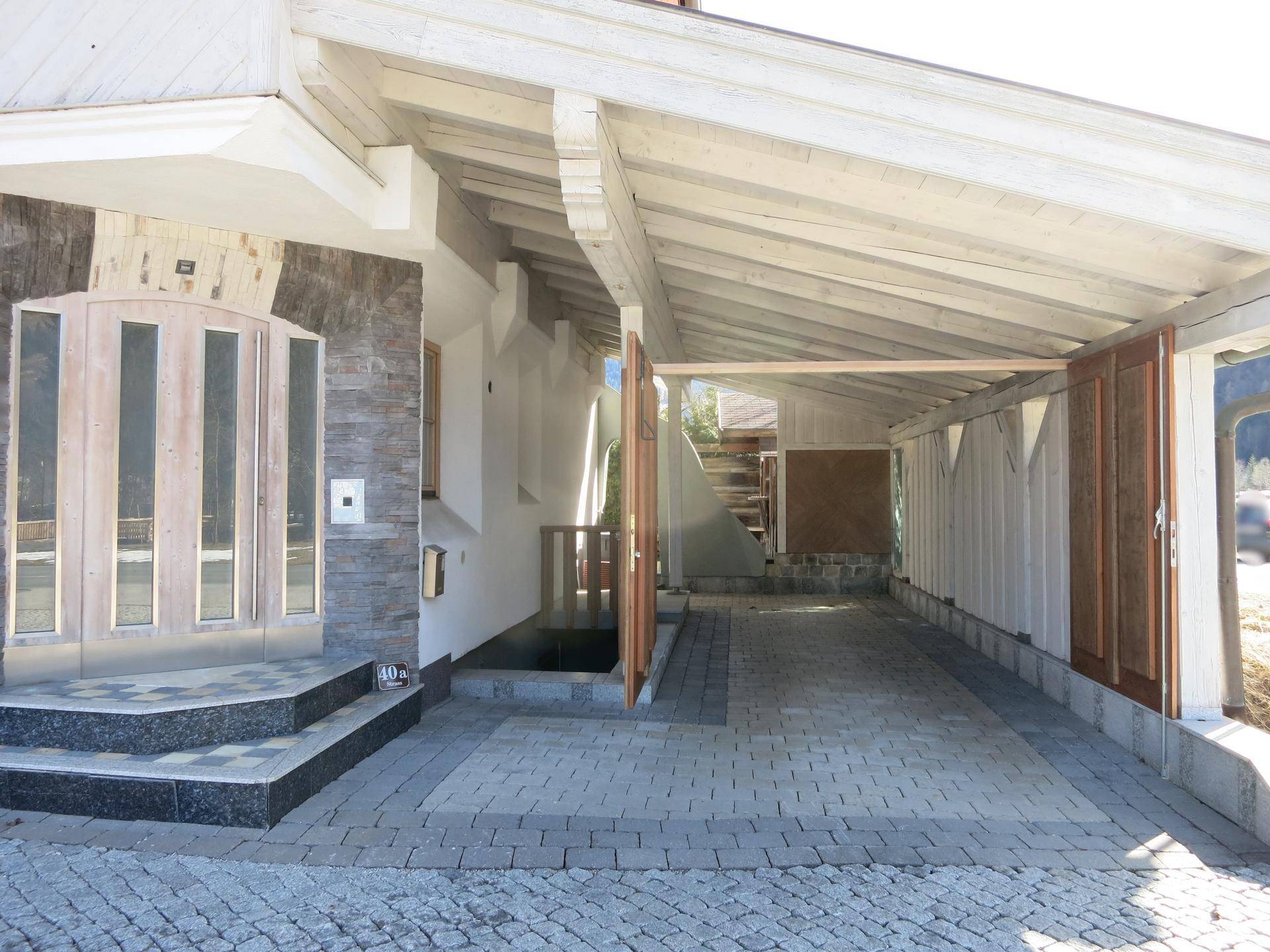 Offener Carport mit weit geöffneten Holztüren, der einen geräumigen Stellplatz bietet.
