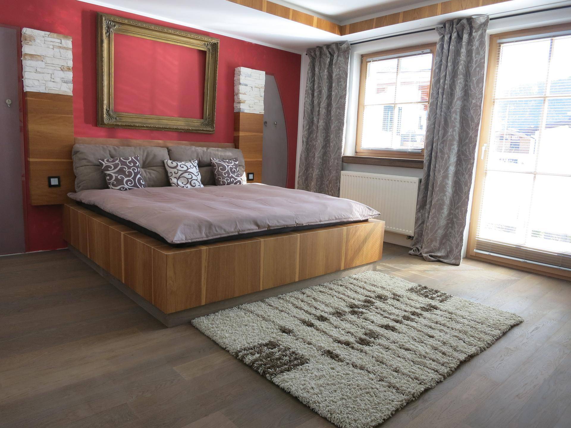 Gemütliches Schlafzimmer mit Holzbett, roter Akzentwand und großem Fenster.