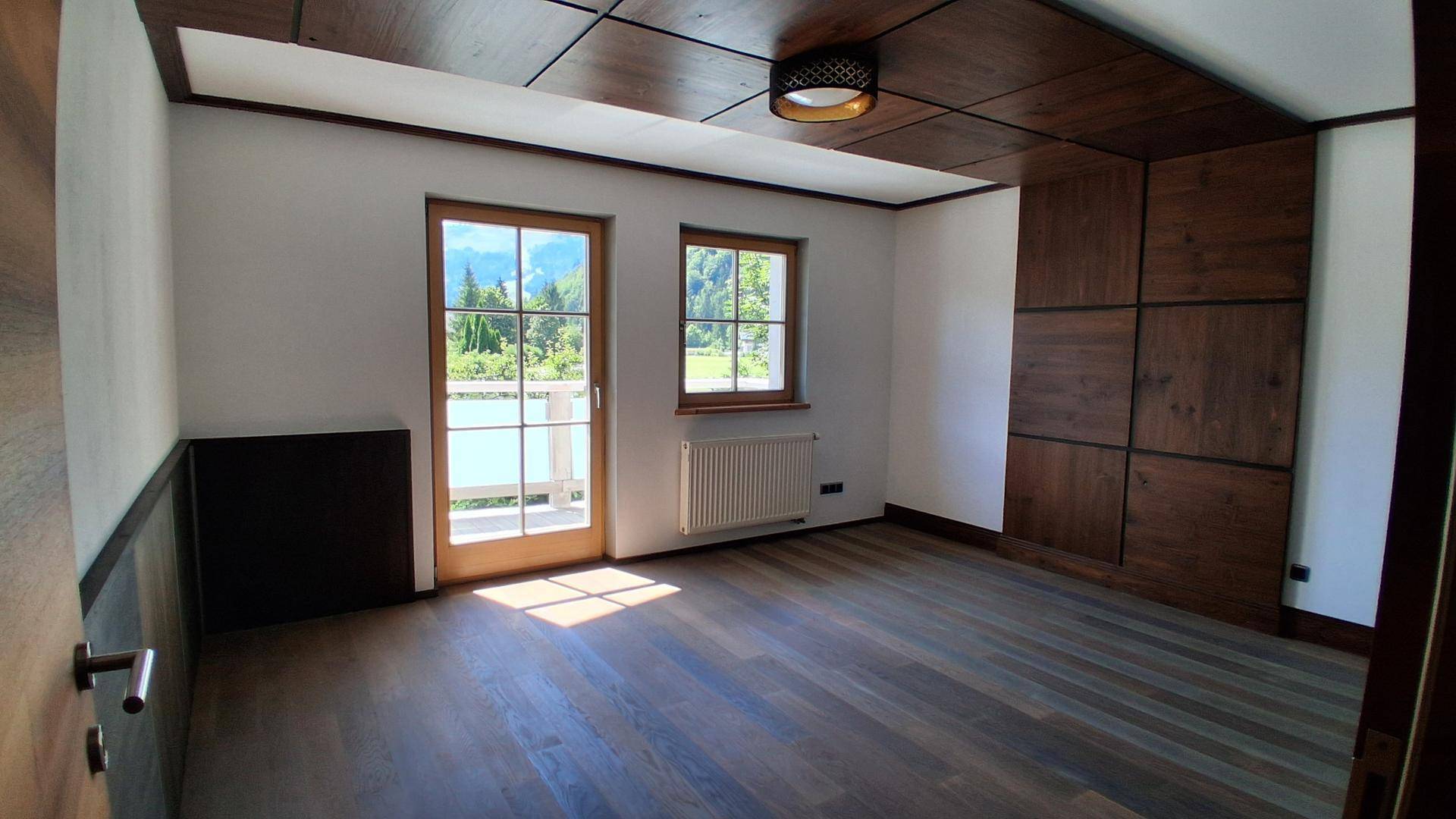 Helles Schlafzimmer mit Holzboden, Holzwandverkleidung und Zugang zum Balkon.