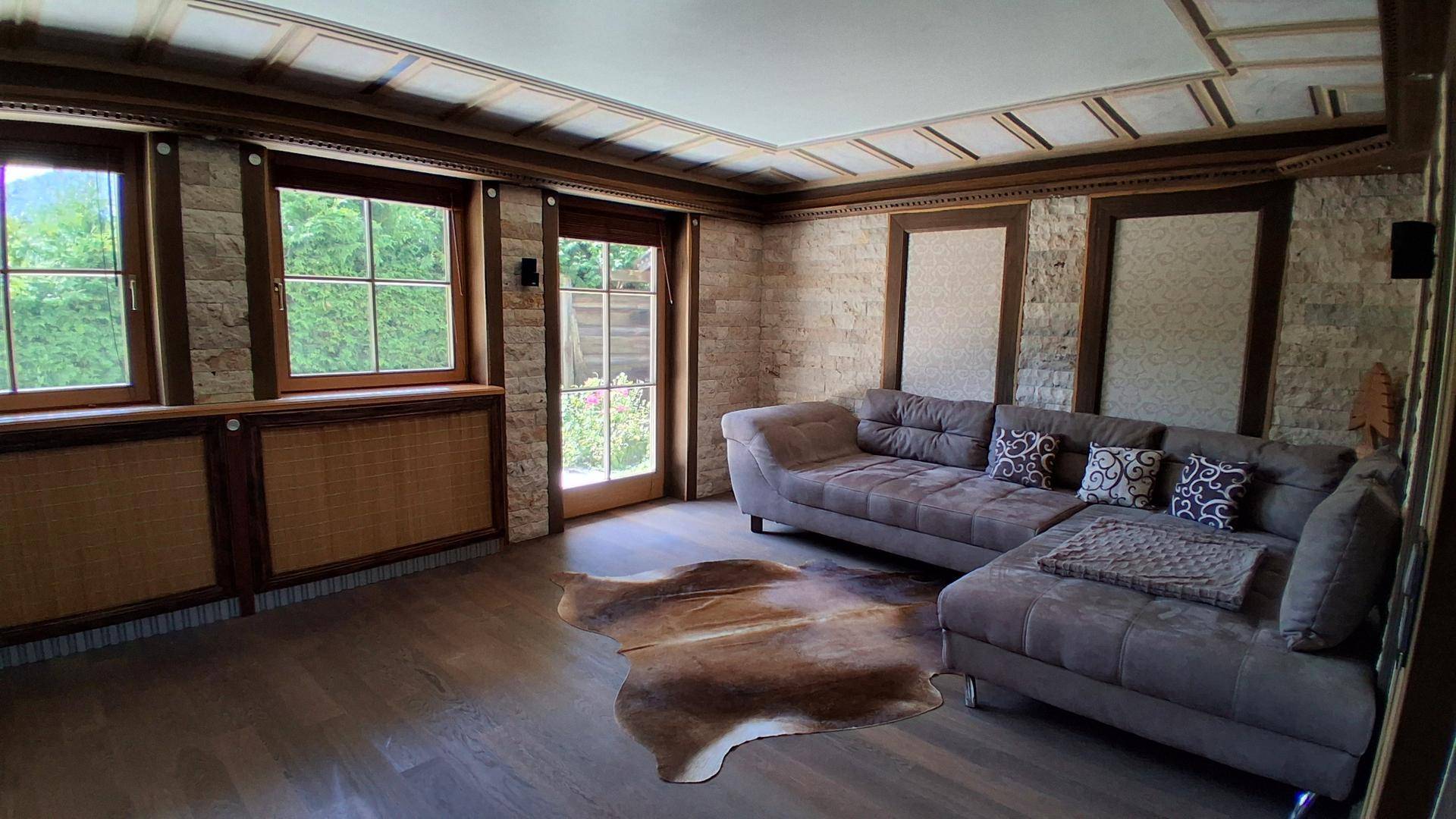 Geräumiges Wohnzimmer mit bequemer Couch, Holzboden und Blick ins Grüne.