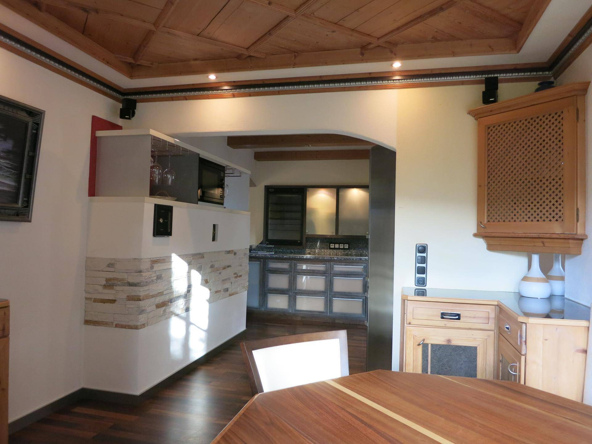Offener Wohn- und Essbereich mit Holzboden und Decke, der in eine moderne Küche übergeht.