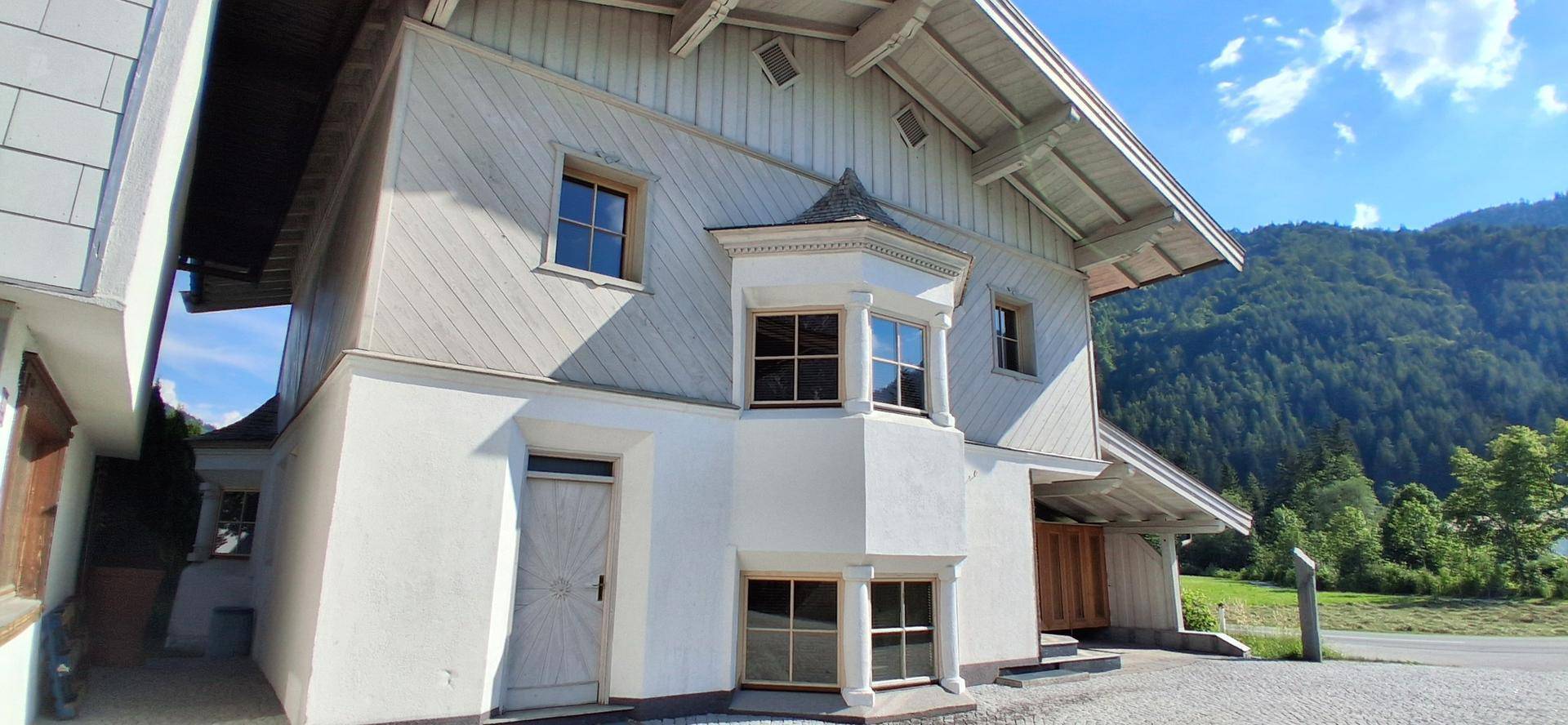 Charmantes Haus mit Erker und Holzelementen vor einer grünen Bergkulisse.