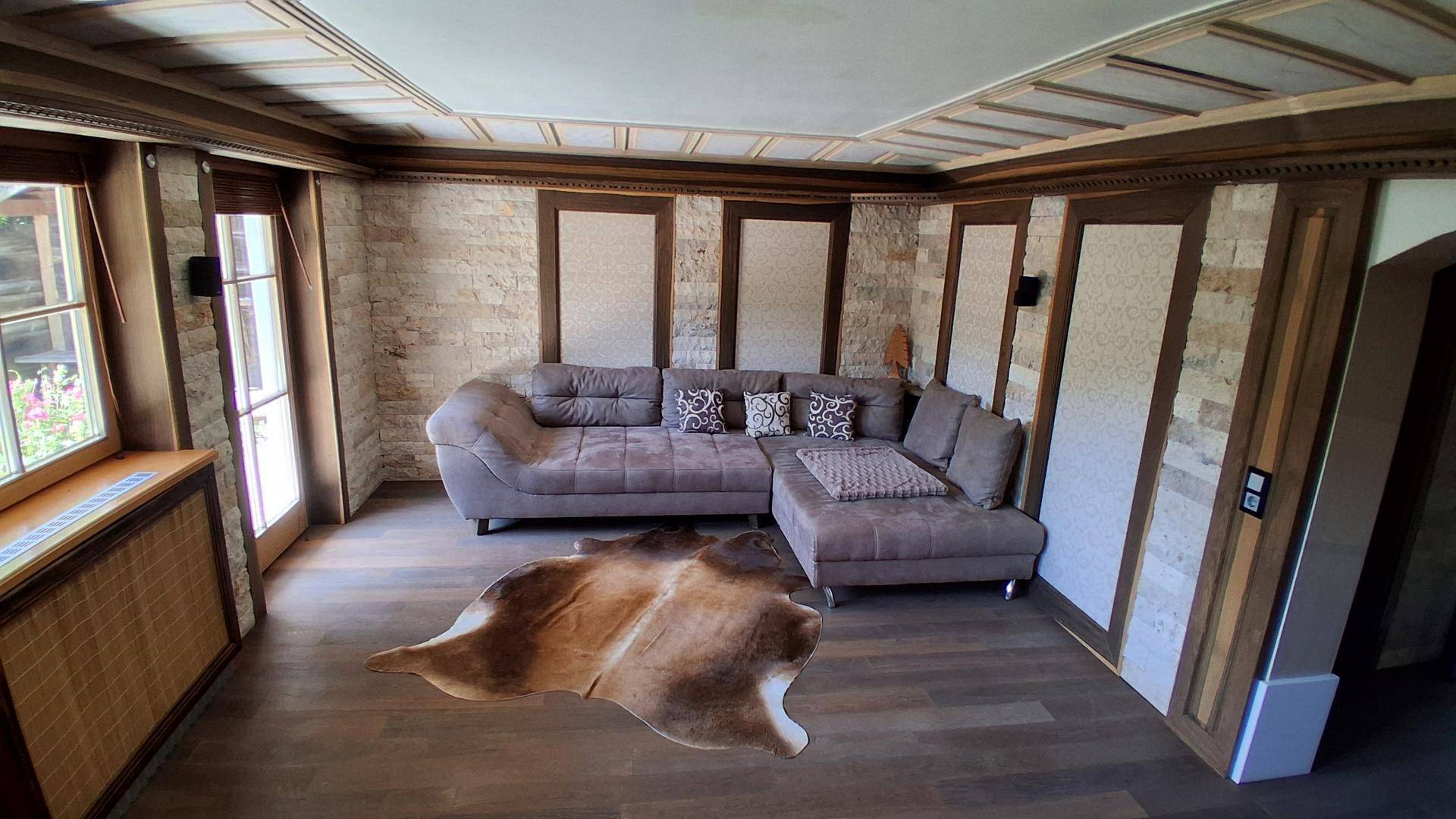 Gemütliches Wohnzimmer mit großem Ecksofa, Holzboden und Steinwandelementen.