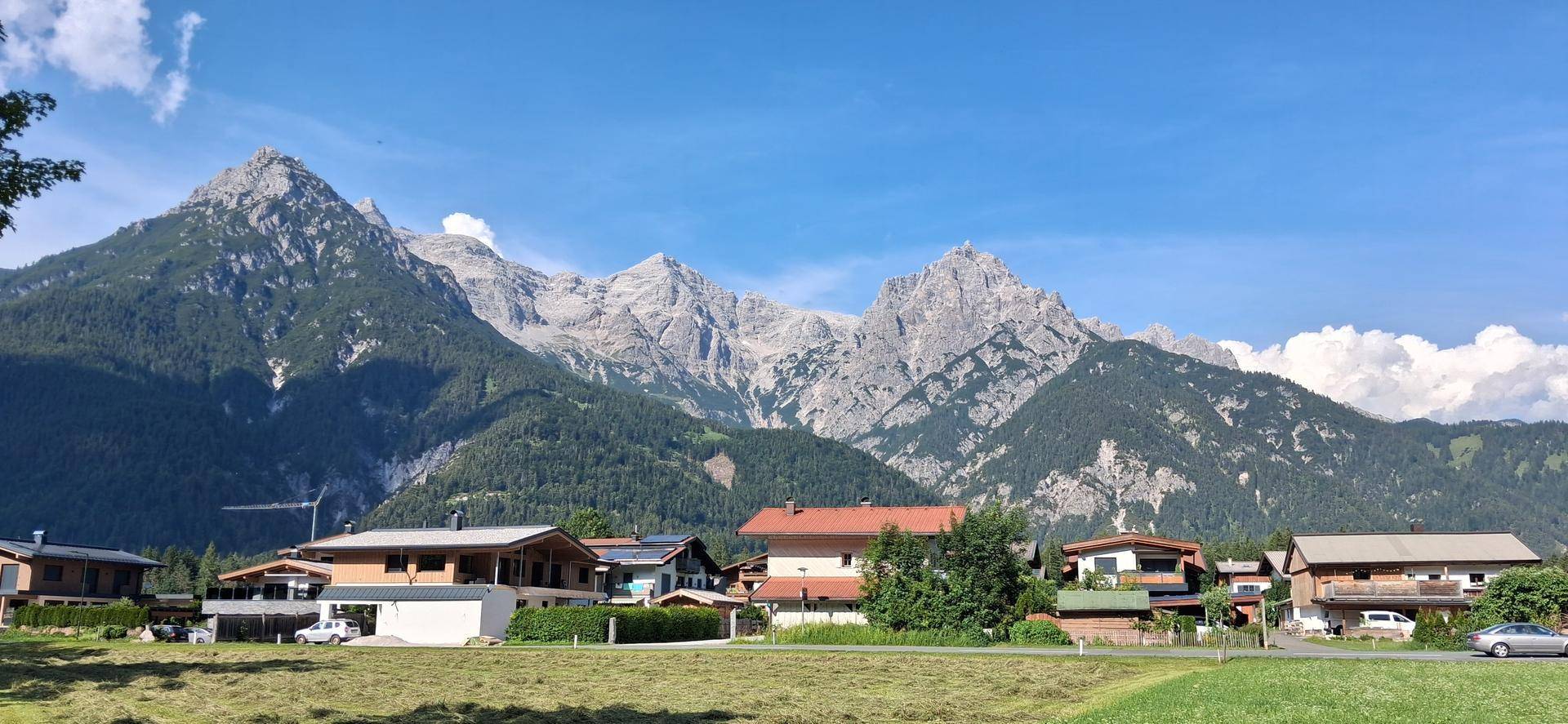 Malerisches Dorf mit Häusern und weiten Feldern vor der beeindruckenden Kulisse majestätischer Berge.