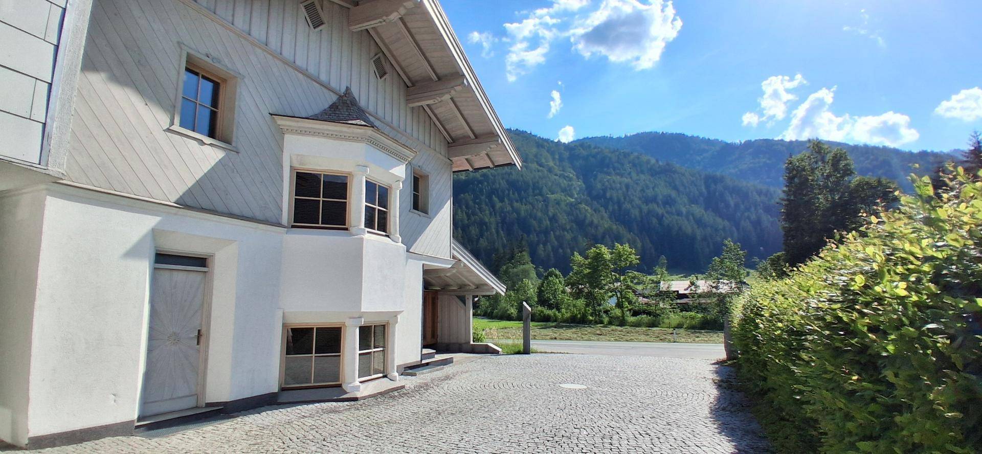Attraktives Haus mit Erkerfenstern und traditionellen Holzelementen vor einer beeindruckenden Bergkulisse.