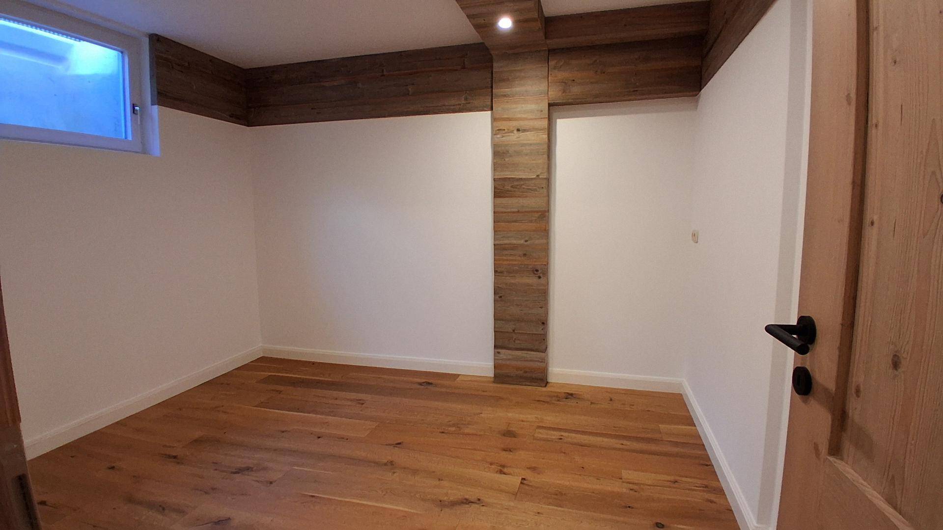 Leeres Zimmer mit hellem Holzplankenboden, weißen Wänden und dekorativen Holzdetails an der Decke.