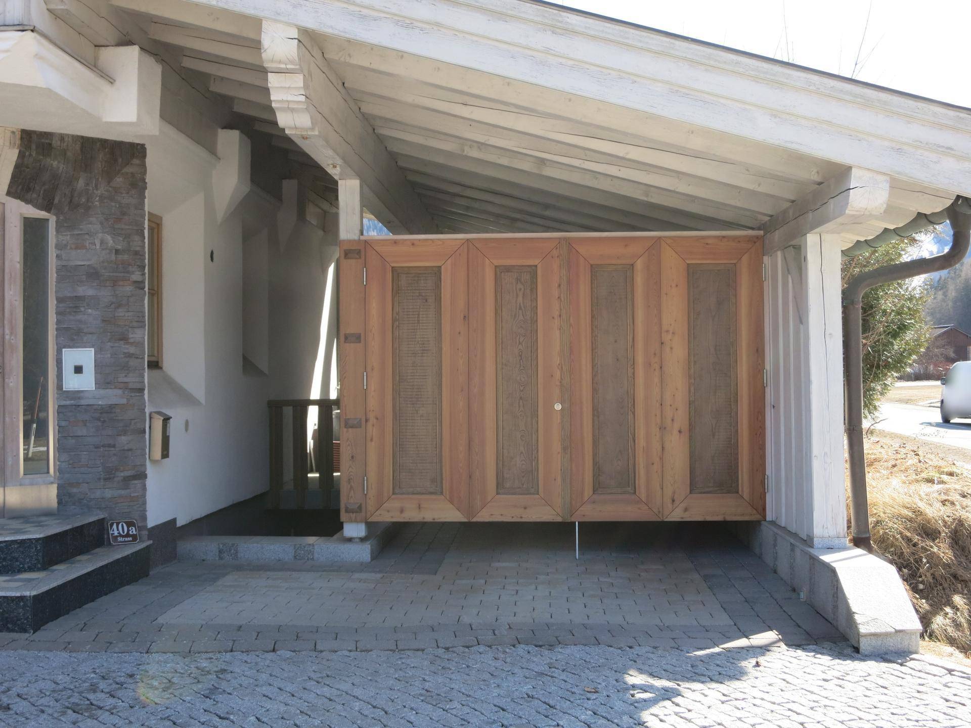Überdachter Carport mit eleganten Holzfalttüren und gepflasterter Zufahrt zum Haus.
