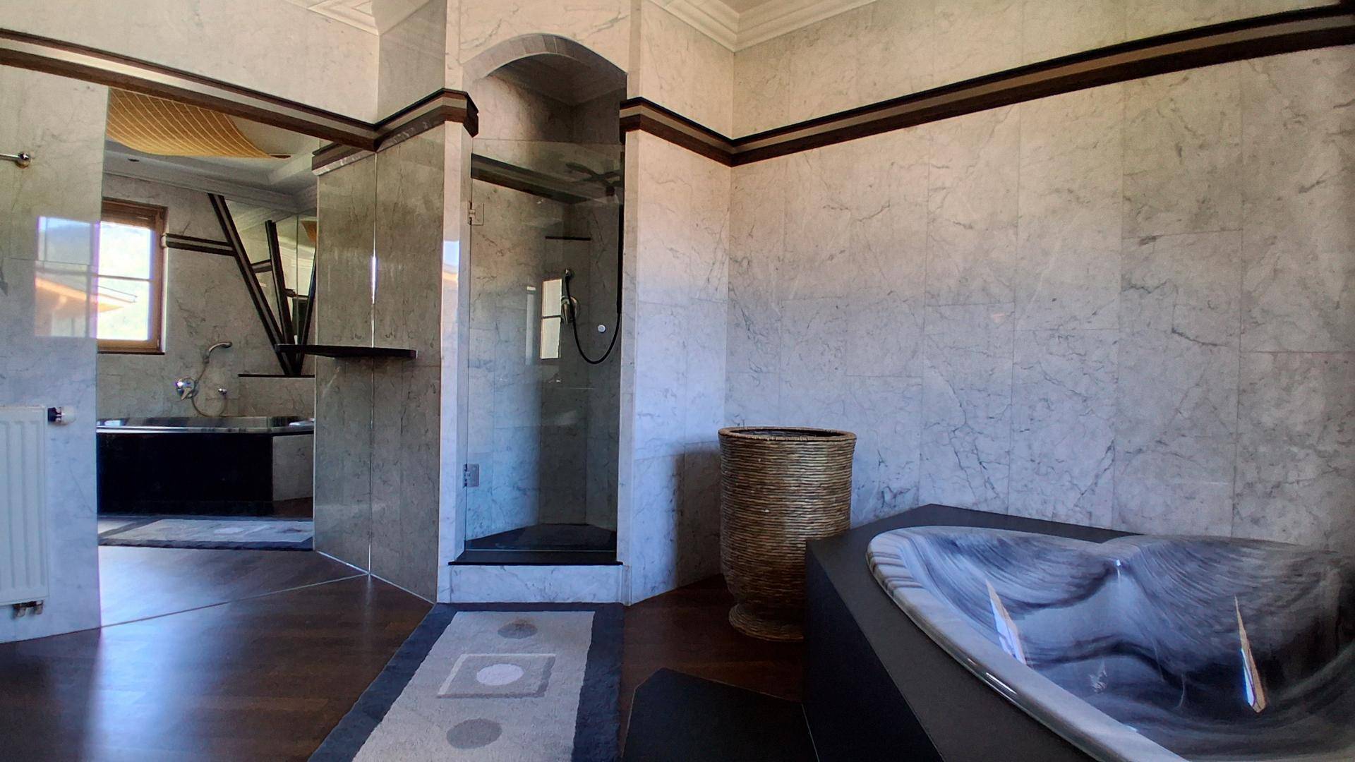 Elegantes Badezimmer mit Marmorwänden, Glasdusche und integrierter Badewanne.