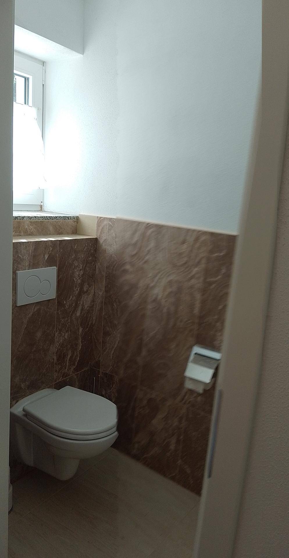 Modernes Gäste-WC mit Wand-WC, braunen Fliesen und Fenster für Tageslicht.