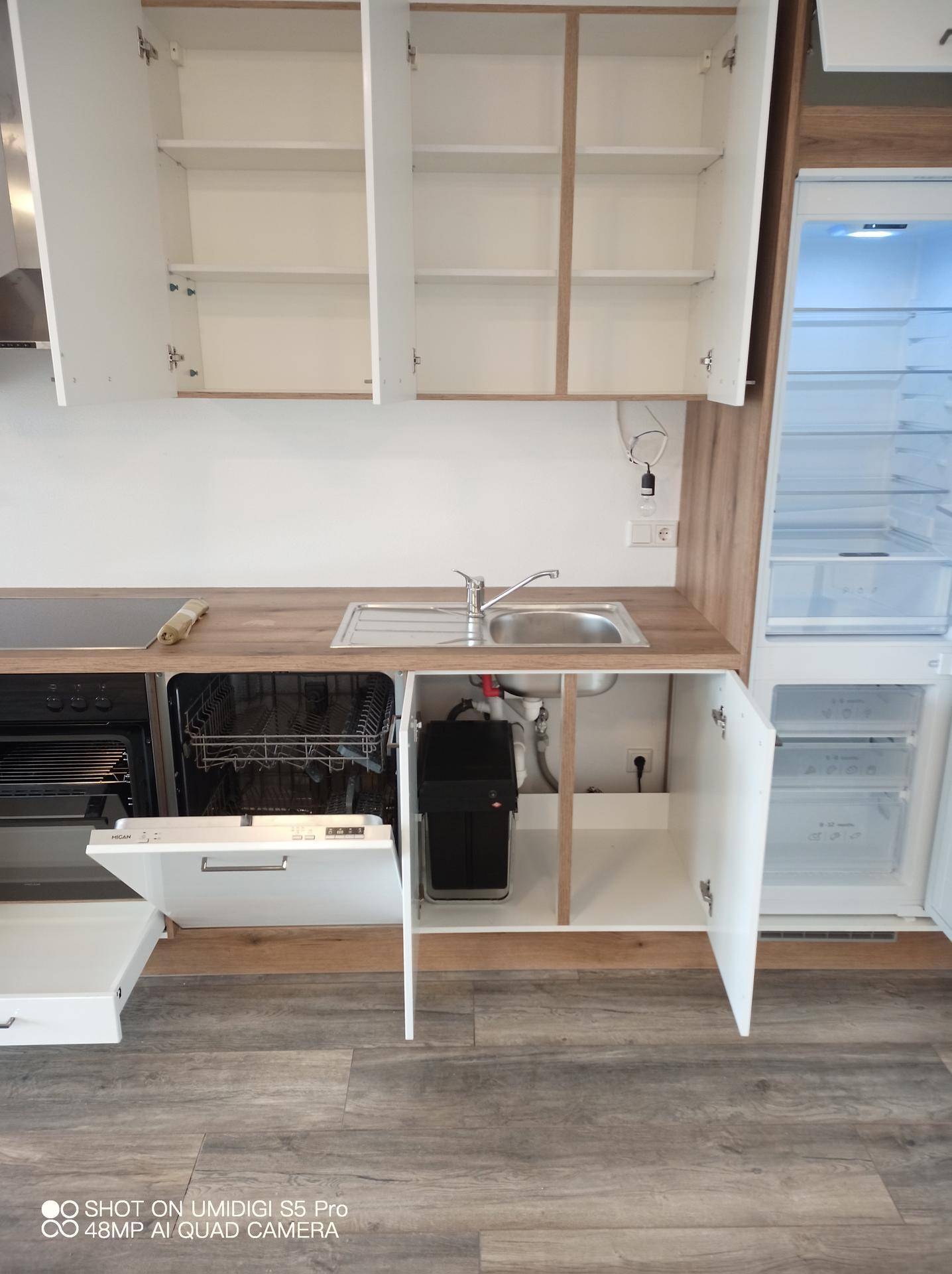 Neue Einbauküche mit Spüle, Geschirrspüler und Holz-Arbeitsplatte in hellem Design.