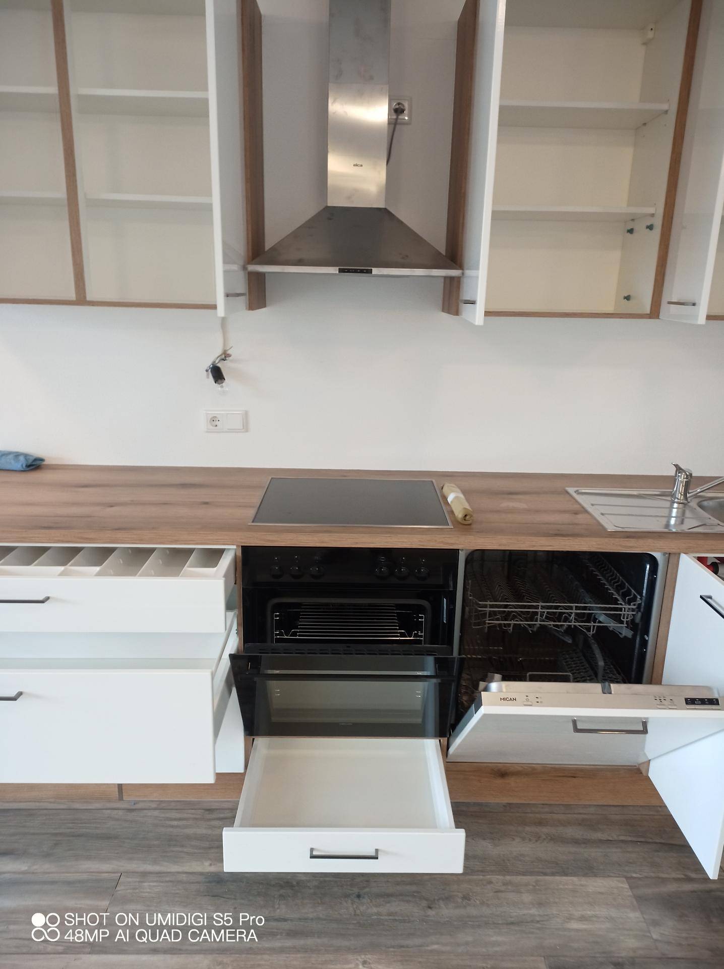 Moderne Küche mit Backofen, Kochfeld und Dunstabzugshaube, bereit für den ersten Gebrauch.