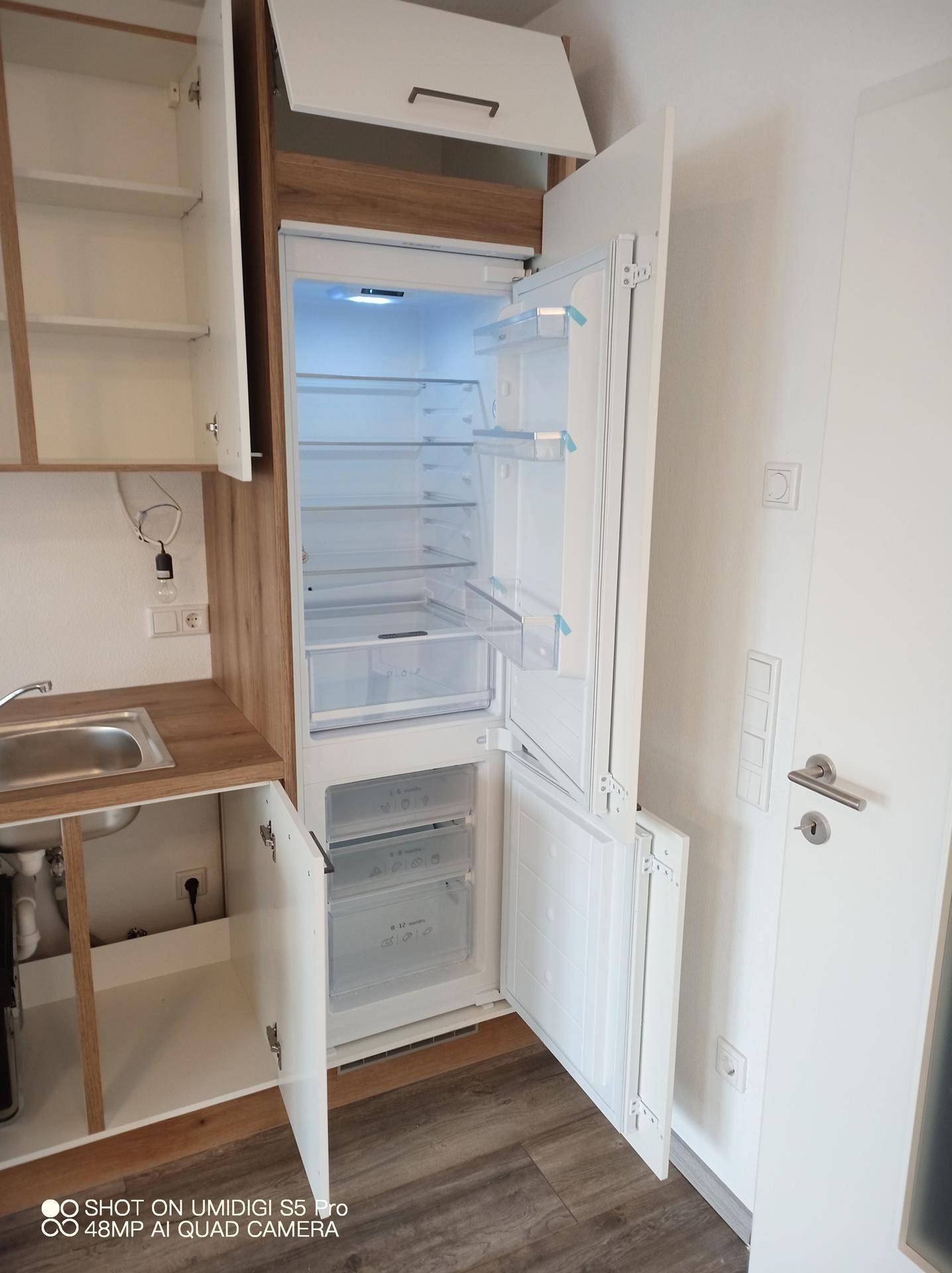 Integrierter Kühlschrank und Gefrierschrank in einer neuen Küche mit Holz- und Weißtönen.