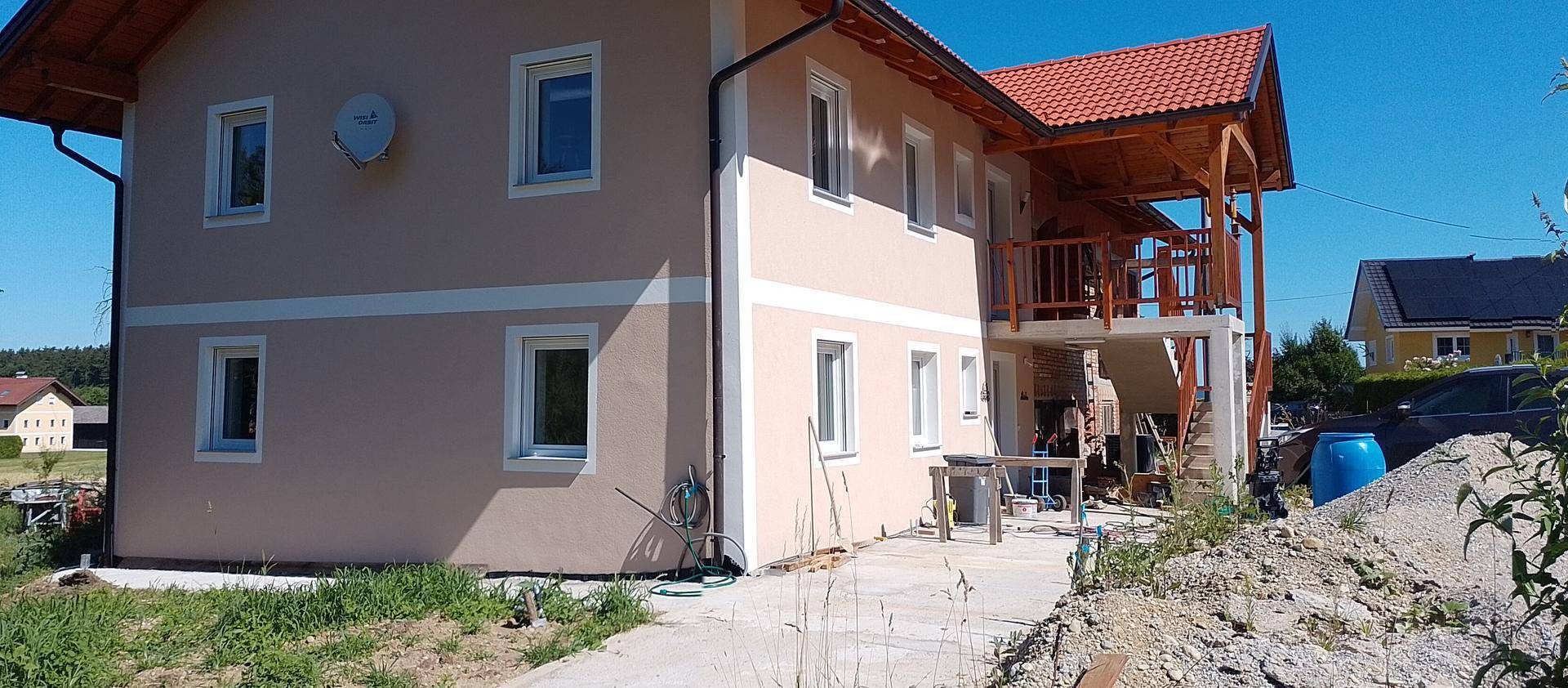 Seitenansicht eines modernen Hauses mit Balkon und rotem Ziegeldach in ländlicher Umgebung.