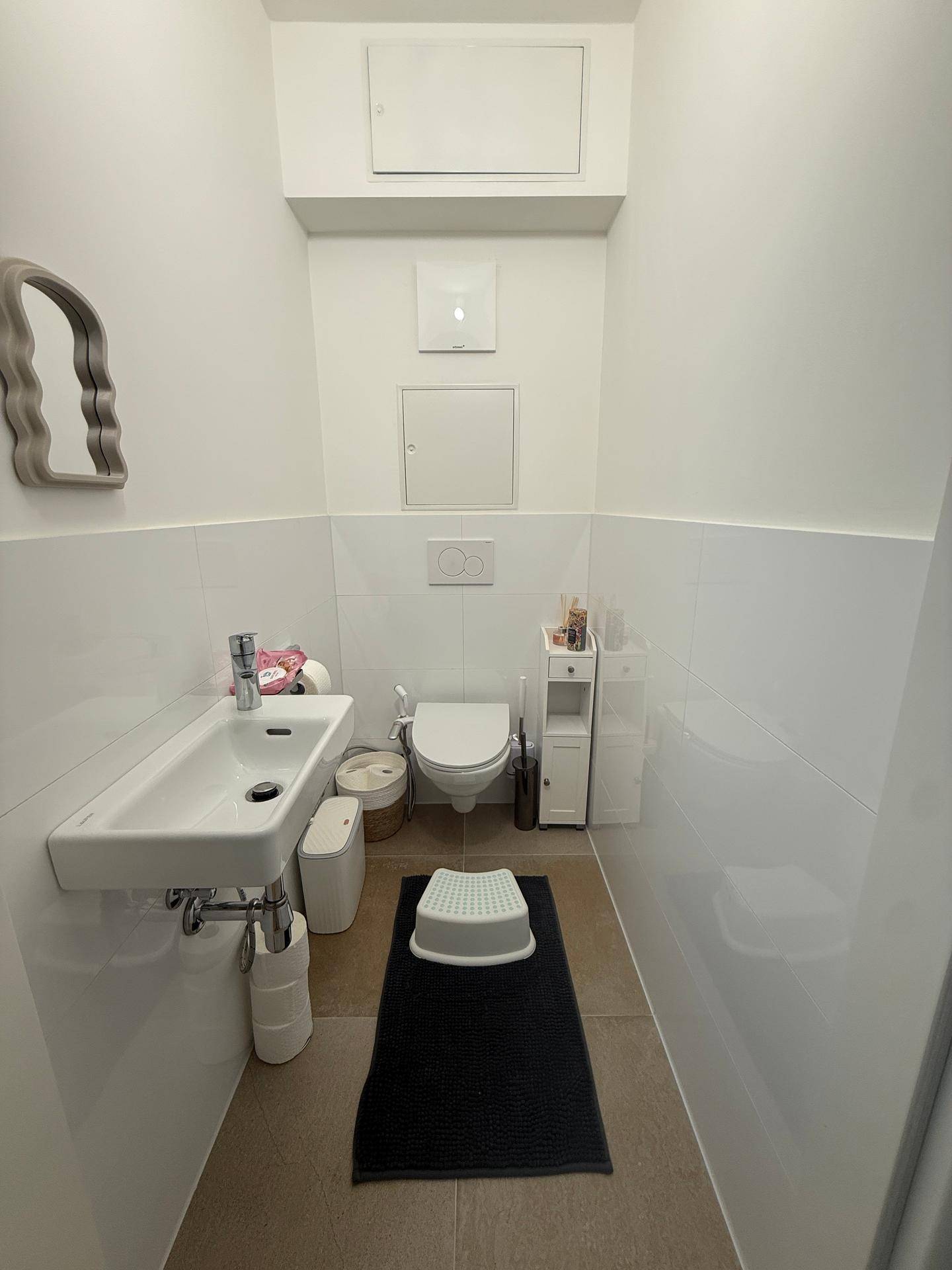 Modernes Gäste-WC mit weiß gefliesten Wänden, kleinem Waschbecken und Wand-WC.