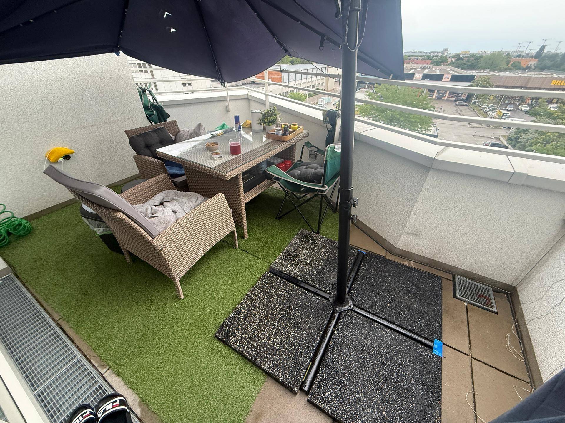 Möblierter Balkon mit Kunstrasen, Sonnenschirm und Blick auf die städtische Umgebung.