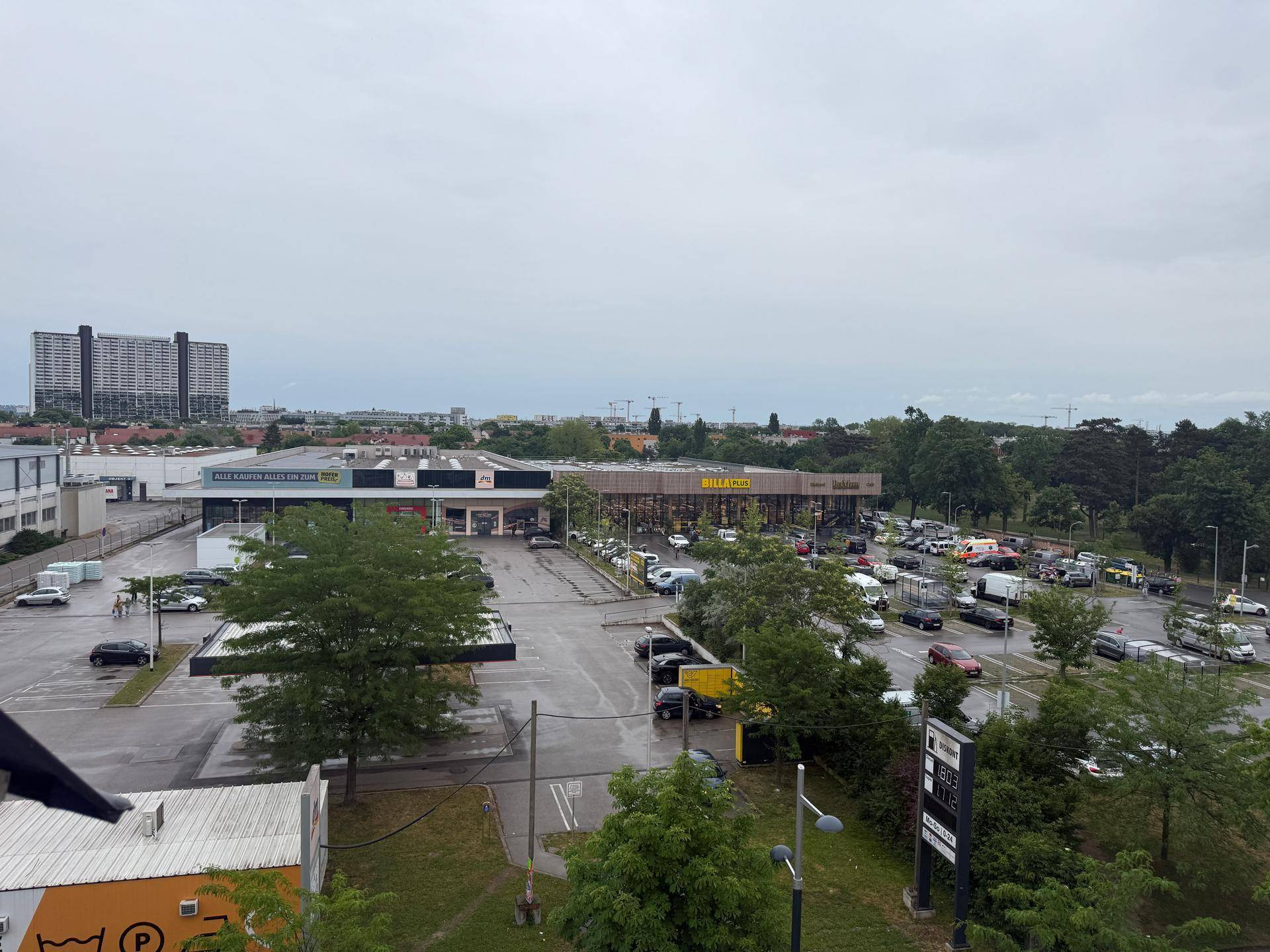 Weitläufiger Blick über eine städtische Umgebung mit Geschäften, Parkplätzen und Grünflächen.
