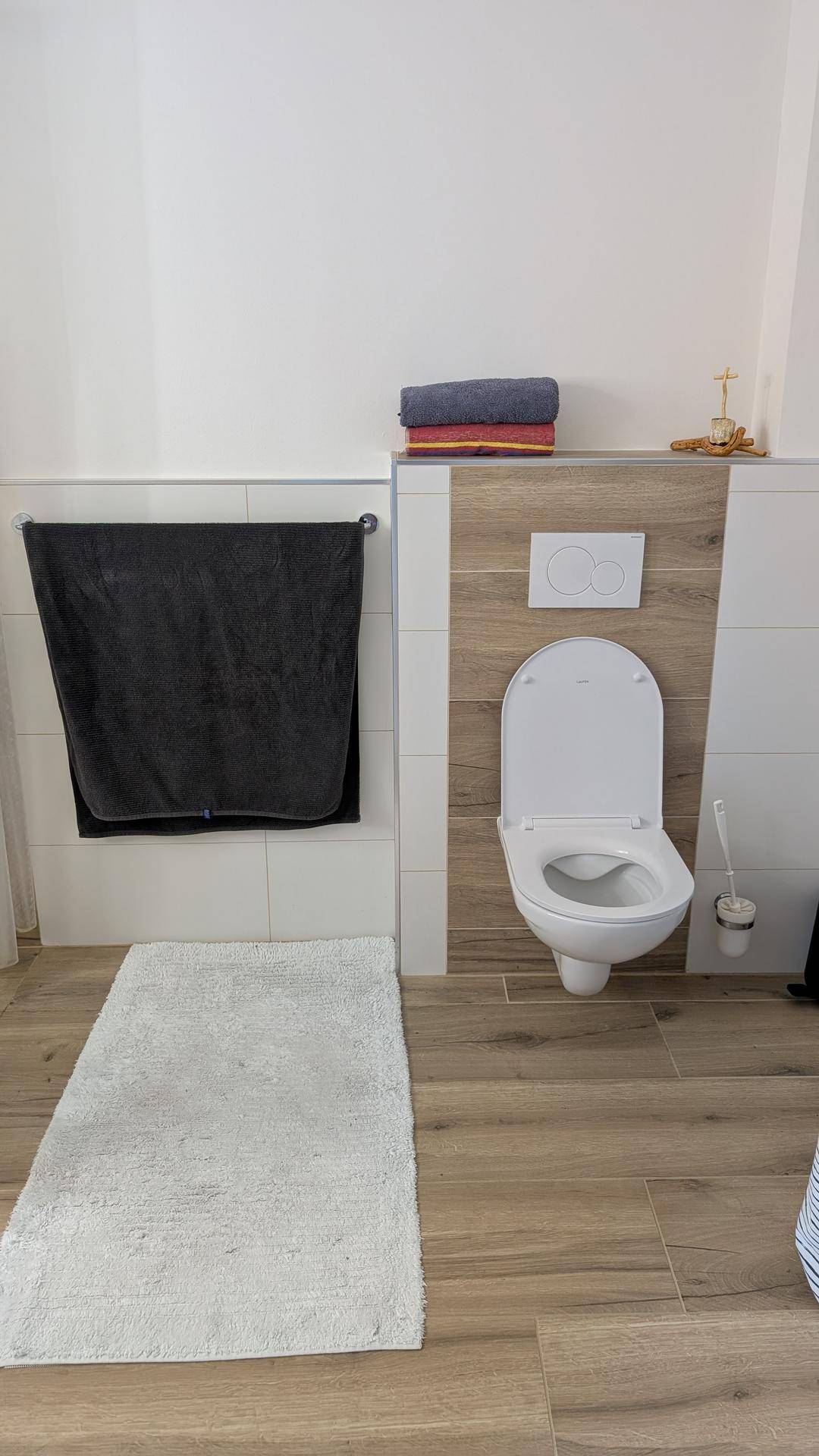 Modernes WC mit wandhängender Toilette und Holzoptik-Fliesen an der Wand.