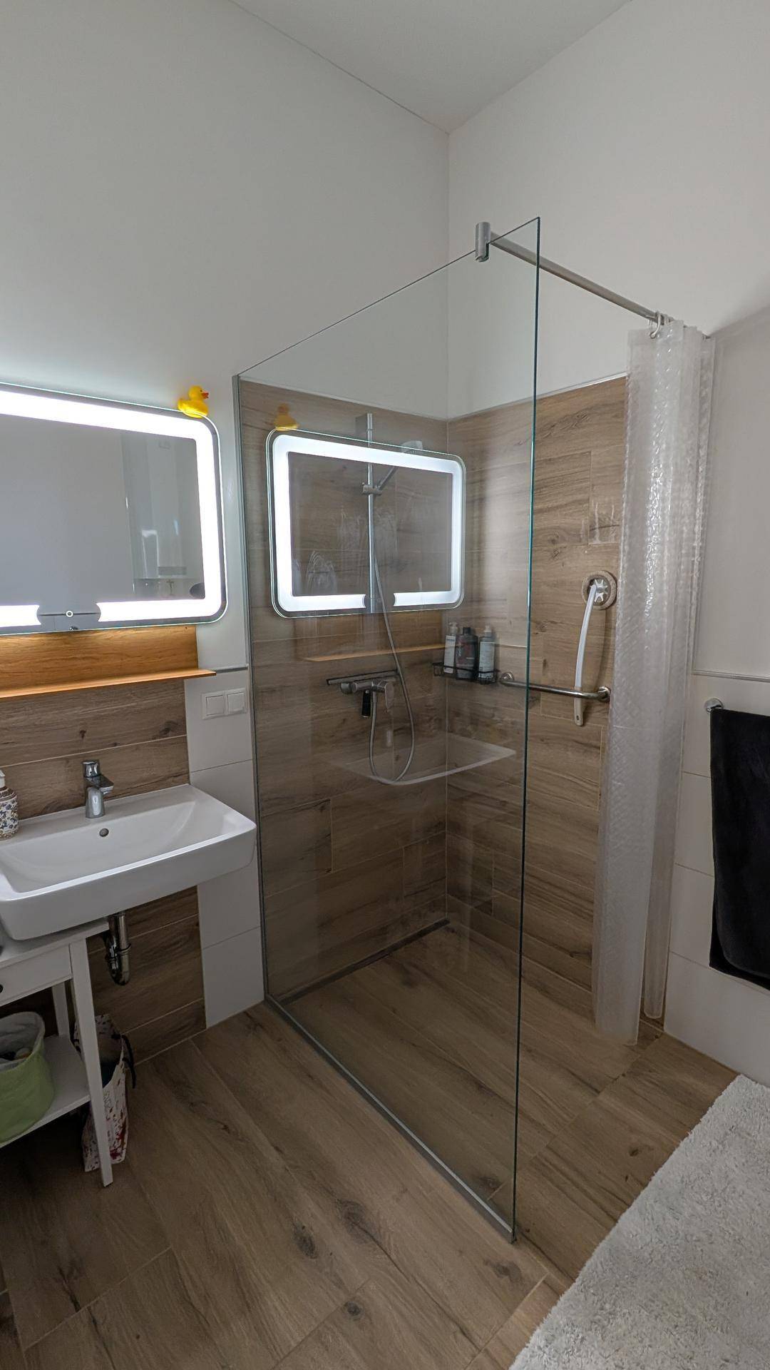 Helles Badezimmer mit moderner Glasdusche, Einzelwaschbecken und beleuchteten Spiegeln.