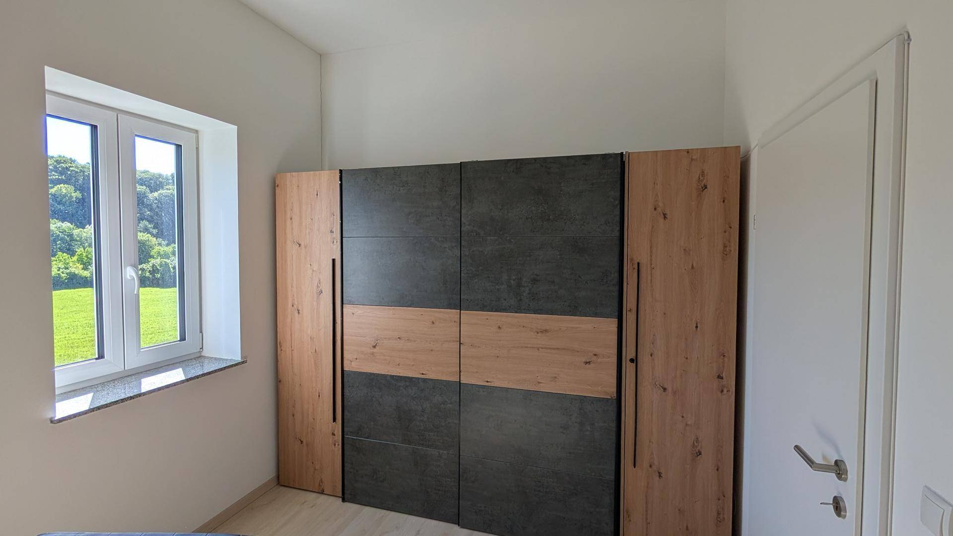 Geräumiger Kleiderschrank mit Holz- und dunklen Paneelen in einem hellen Schlafzimmer mit Fenster.