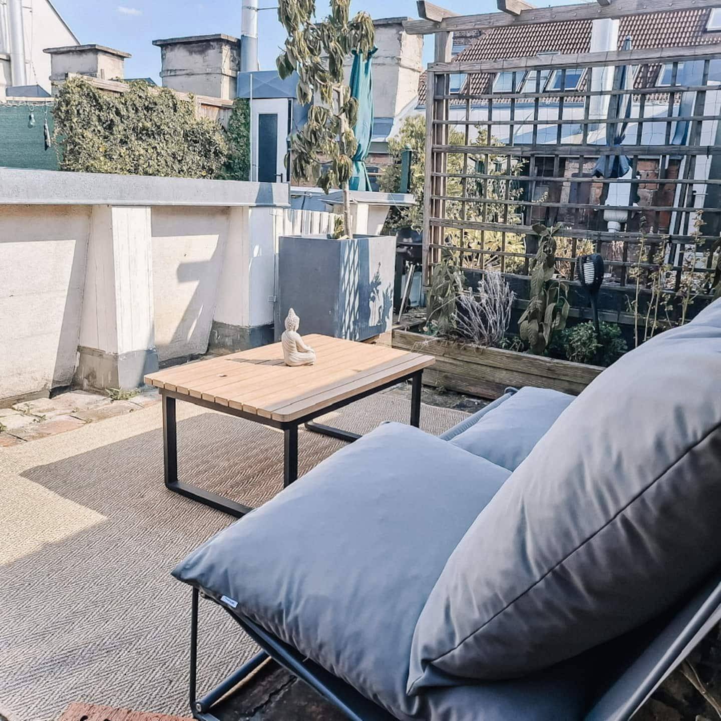 Sonnige Dachterrasse mit bequemen Sitzmöbeln, Holzzaun und Blick ins Grüne.