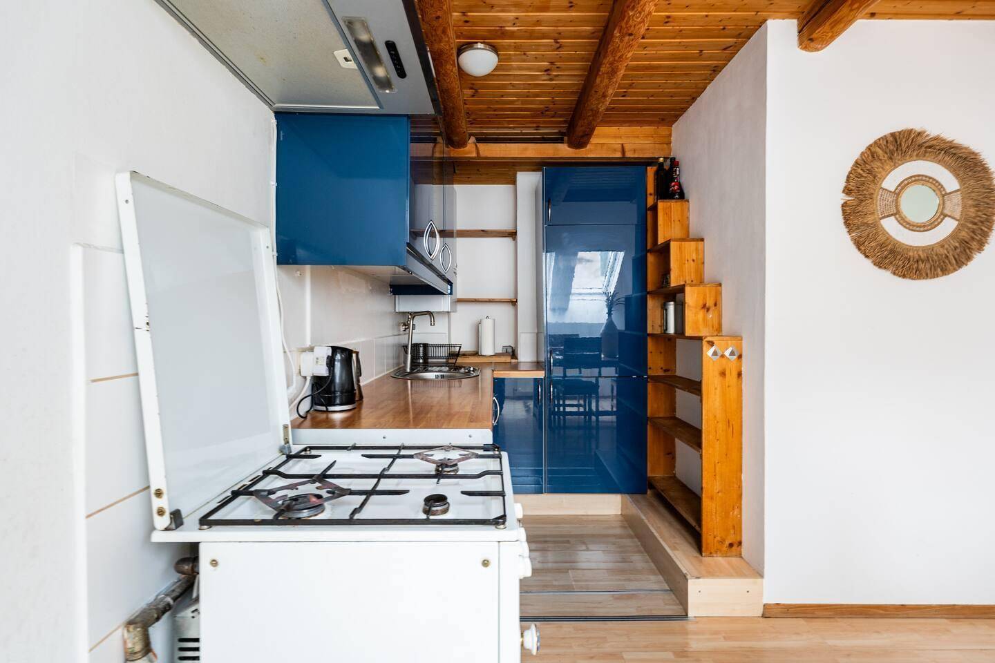 Funktionale Küche mit blauen Hochglanzschränken, Holztheke und Gasherd unter Holzbalken.