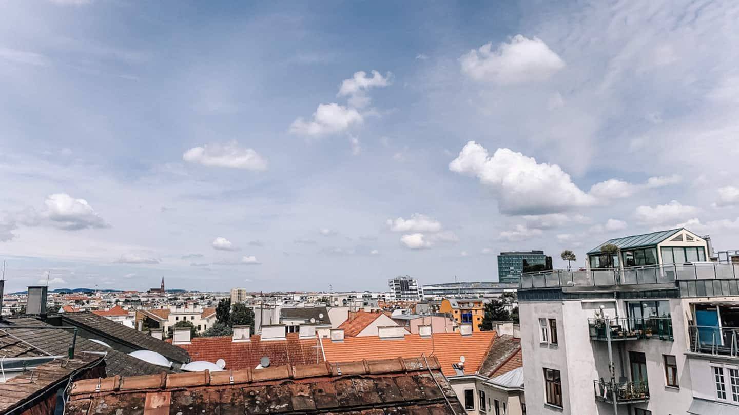 Weitläufiger Blick über die Dächer einer Stadt unter einem bewölkten Sommerhimmel.